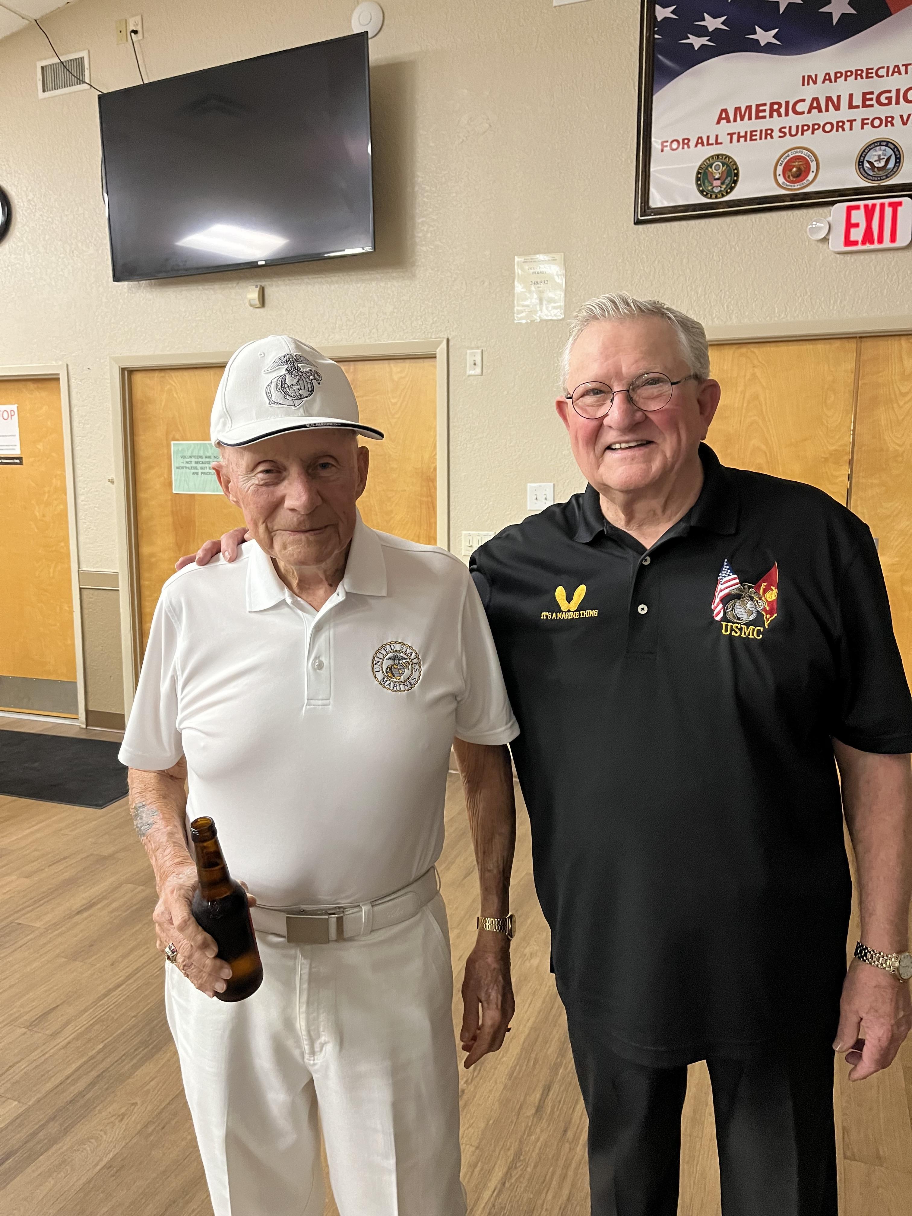 Two older men share a moment of joy at a community center, enjoying drinks and each other's company.