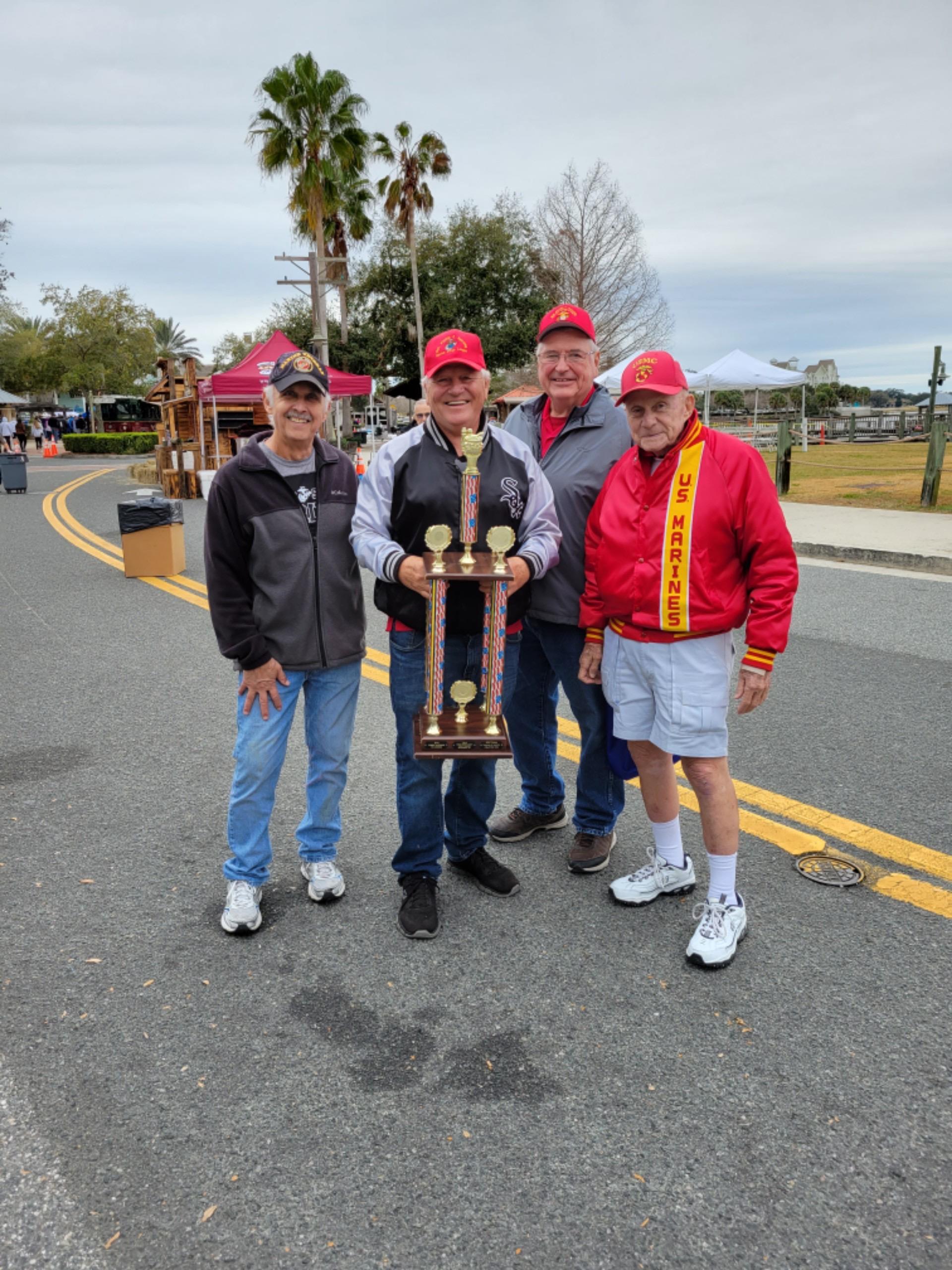 Four men wearing caps and casual clothes celebrate their achievements in a park during an event.