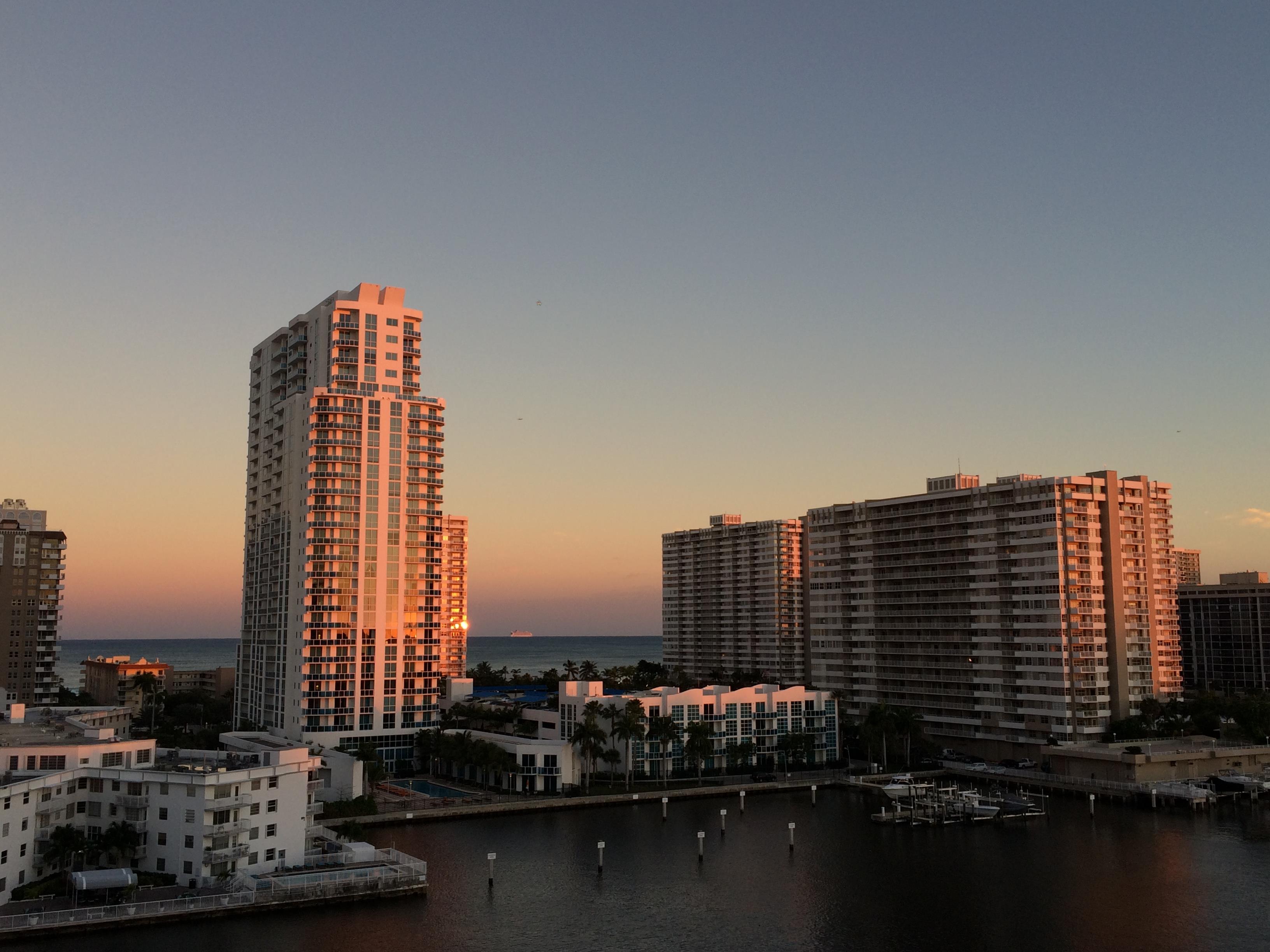 Buildings in a coastal area glow orange under a stunning sunset over the water.