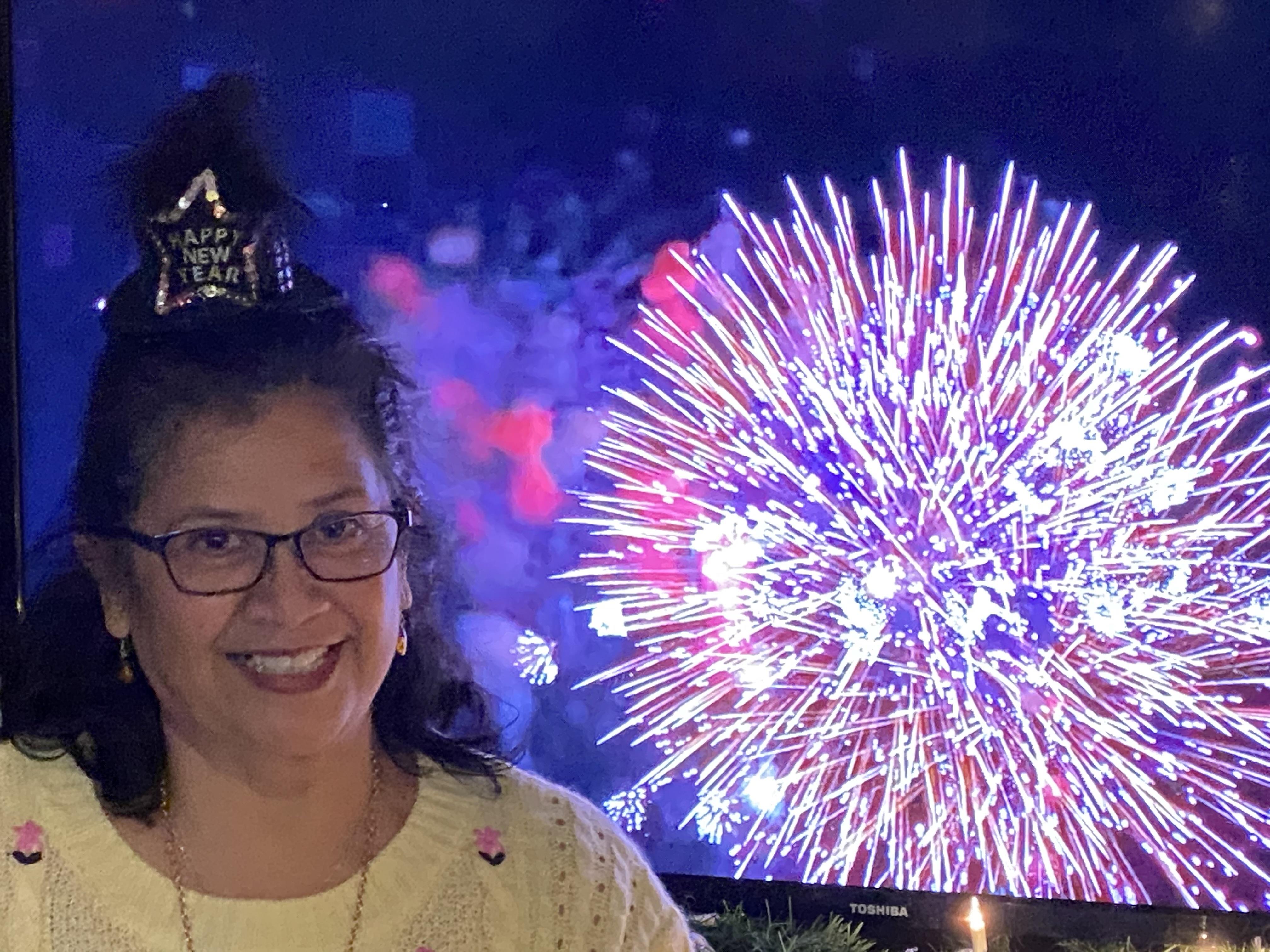 A woman smiles joyfully as colorful fireworks explode in the night sky during a celebration.