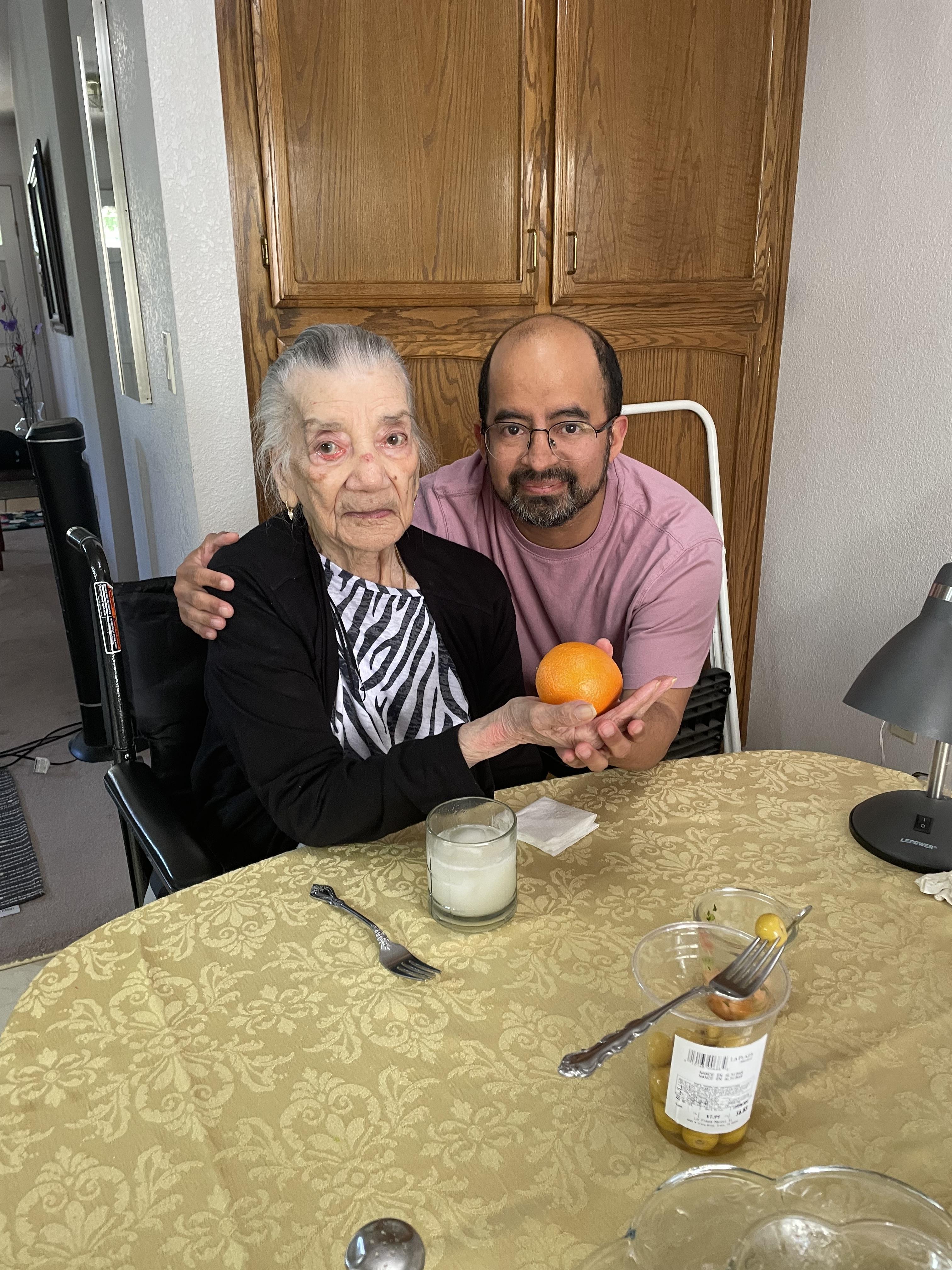 A man and an elderly woman enjoy quality time together at a cozy kitchen table, sharing smiles.