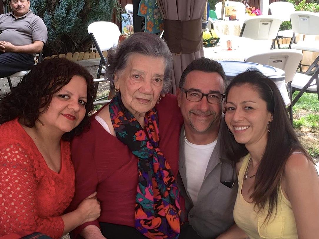 Four family members share smiles and embrace in a pleasant outdoor location during a gathering.
