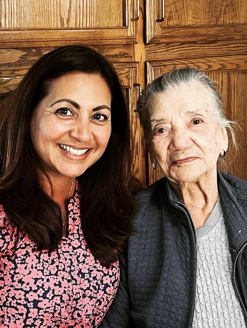 Two women smile happily at the camera, surrounded by a cozy, warm family setting.