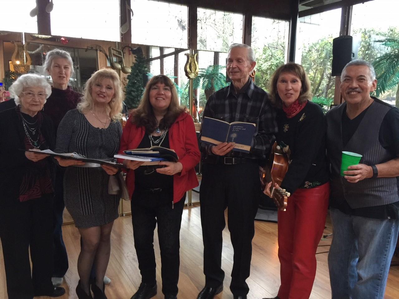 A lively group of six performers stands together, sharing music and laughter in a bright venue.