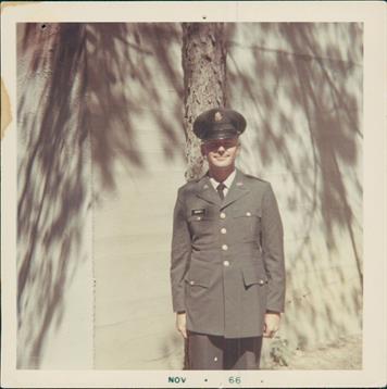 Soldier stands proudly in uniform by a tree, enjoying a sunny day with camaraderie.