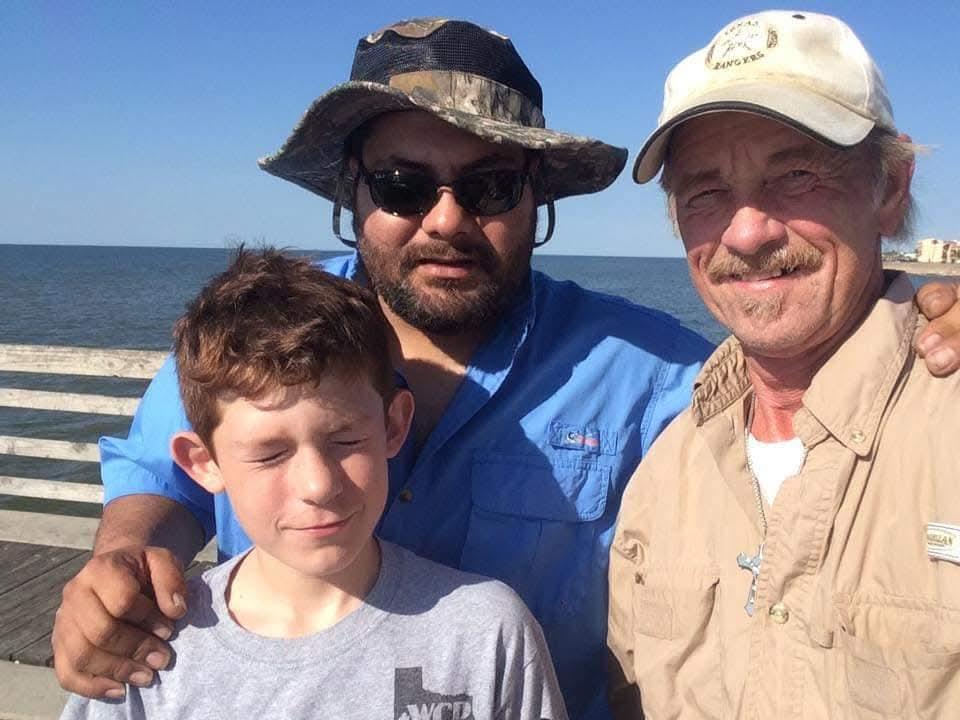 Friends and family pose together on a pier near the ocean on a clear sunny day.