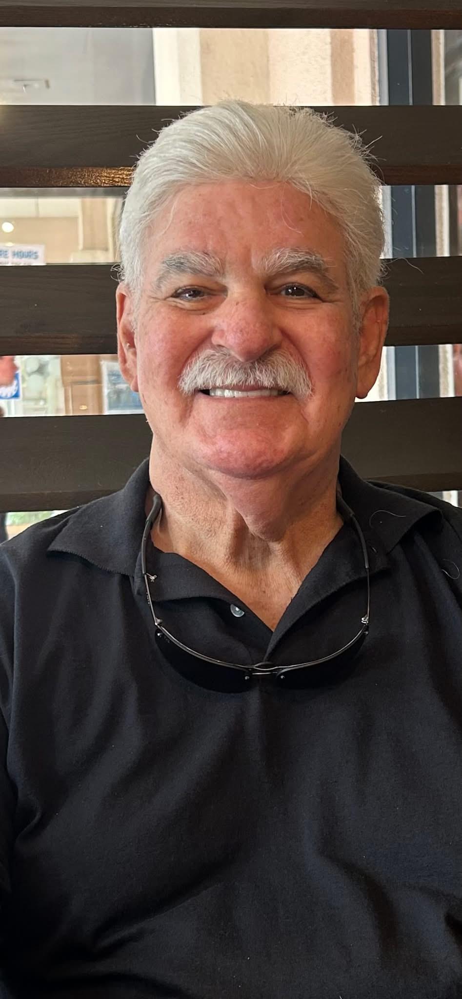 A smiling older gentleman relaxes in a casual setting, enjoying a pleasant day.