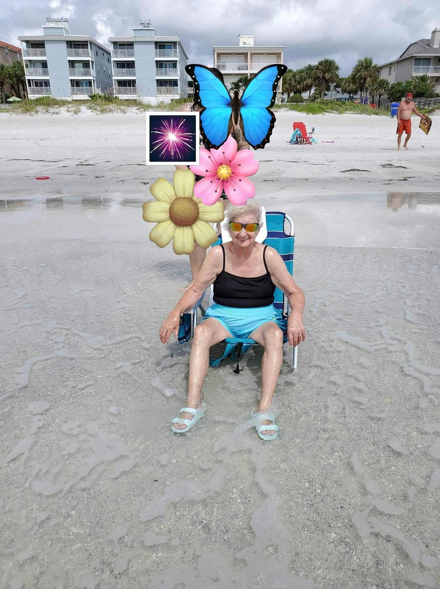 An elderly woman relaxes in a beach chair by the ocean, enjoying the sun and decorations.