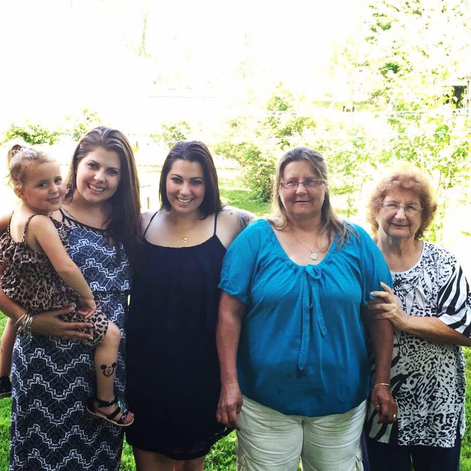 Four women and a girl pose together in a lush green park under bright sunlight.