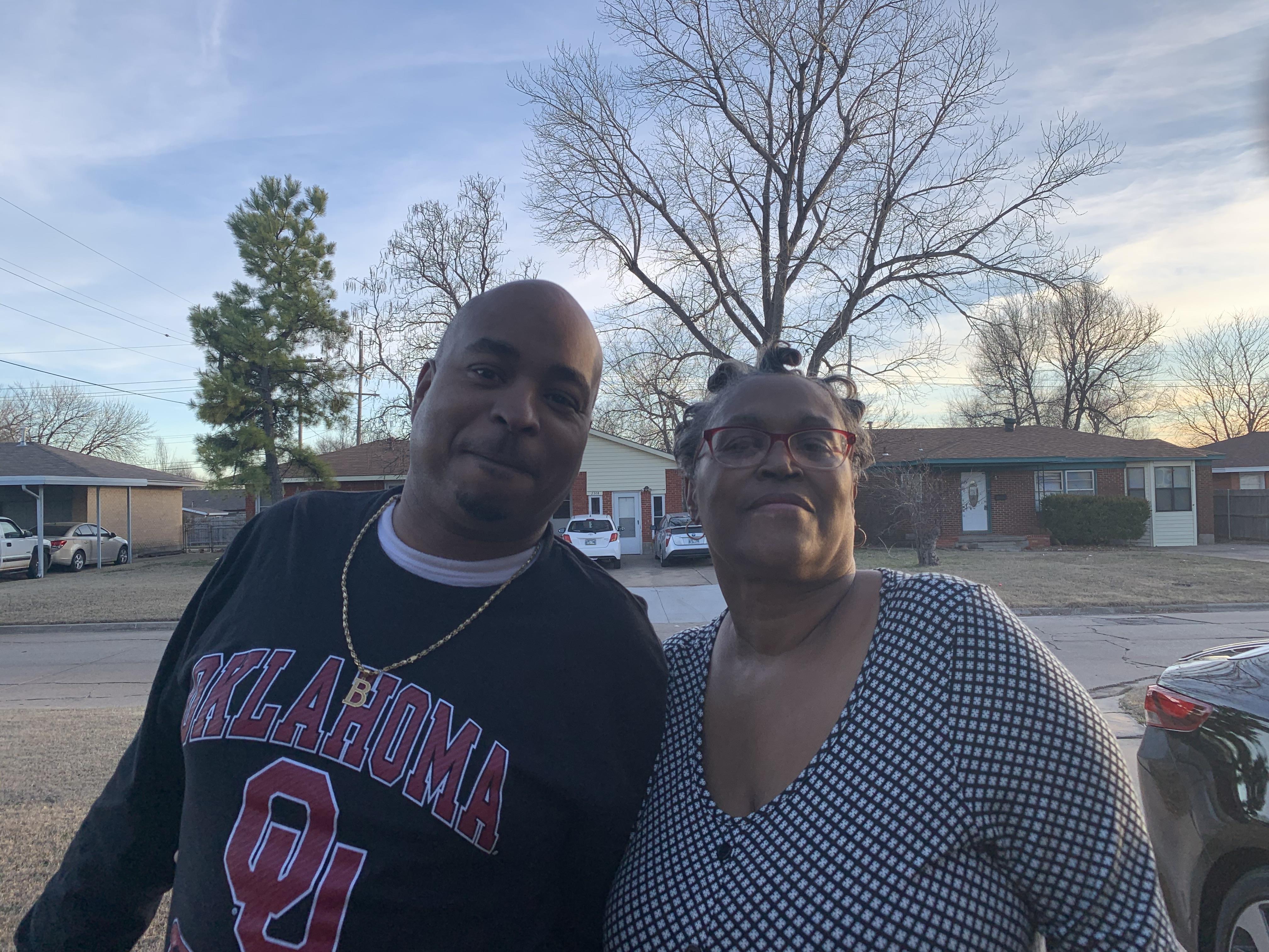 Two friends smile warmly while standing together outdoors on a clear day.