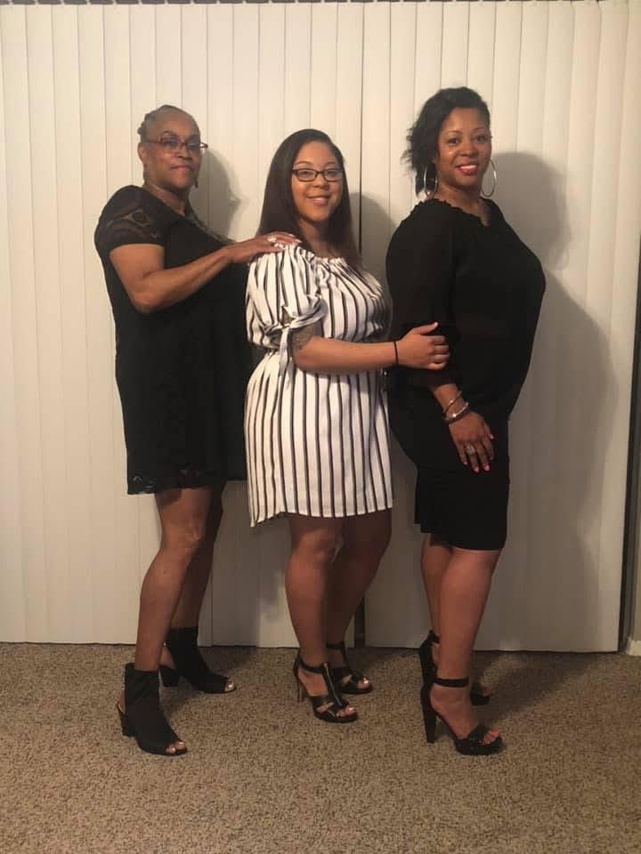 Three women stand together in coordinated outfits, smiling at the camera in a well-lit indoor space.