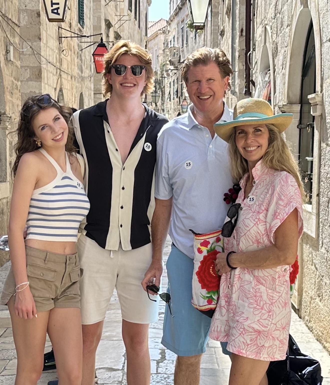 A family poses happily on a sunny day in a picturesque old town, showcasing their stylish outfits.