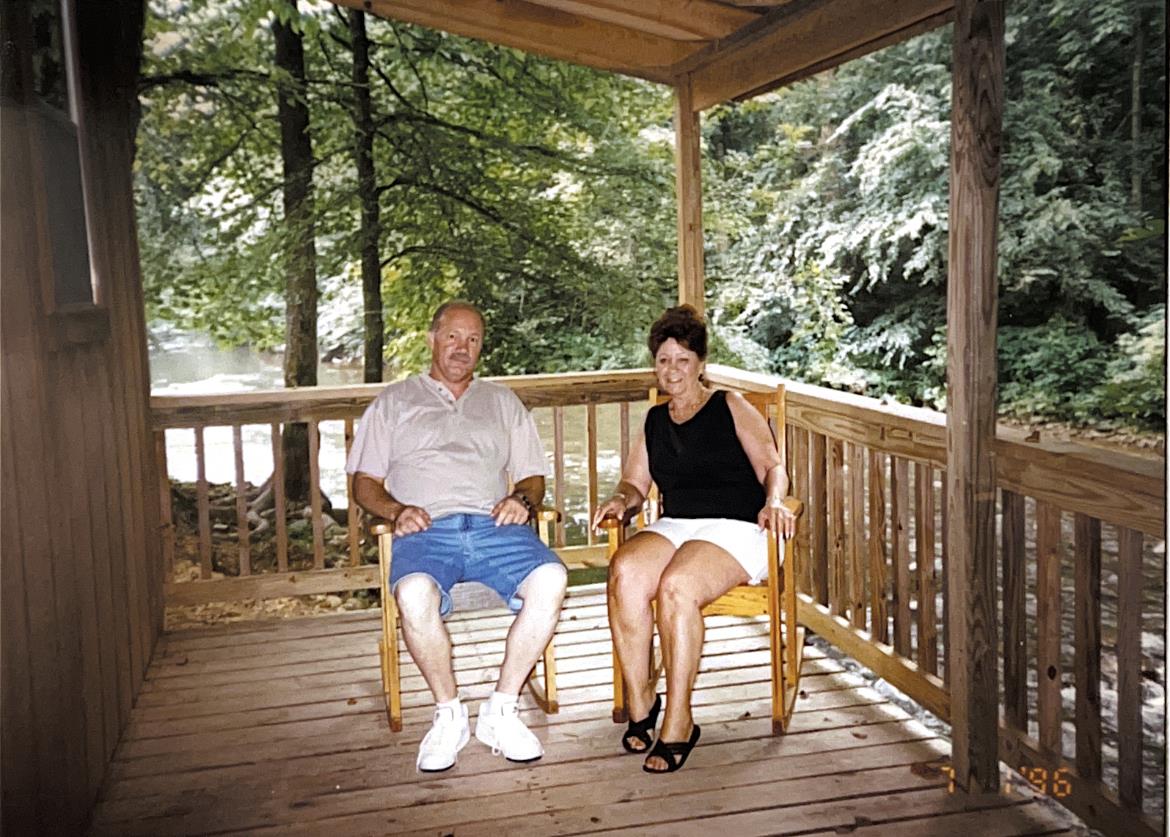 A senior man and woman enjoy their time together on a cozy porch in a natural setting.