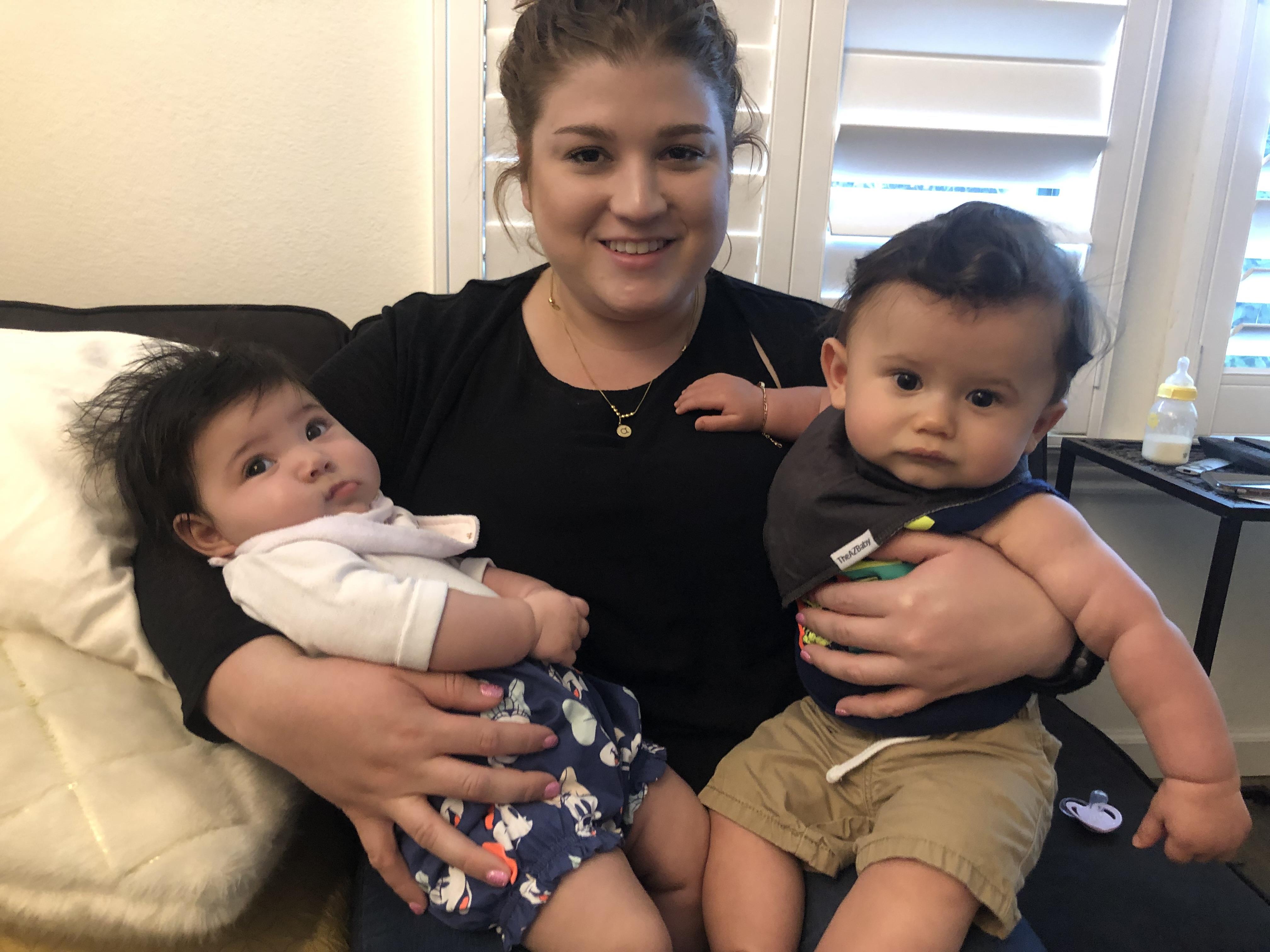 A joyful woman smiles while cradling two babies, creating a heartwarming moment in a cozy setting.