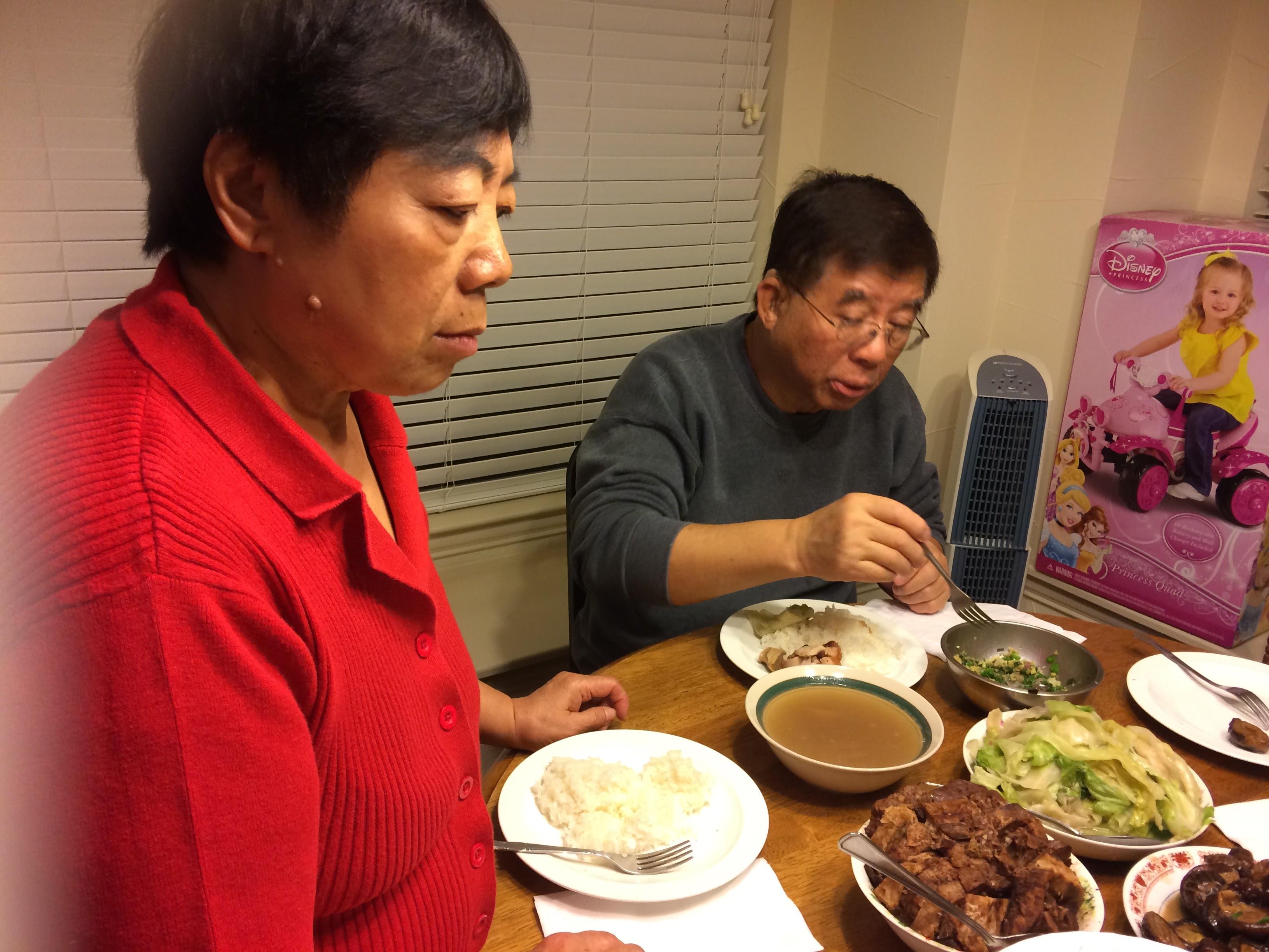 Two people enjoy a hearty meal together at a dining table filled with dishes and rice.