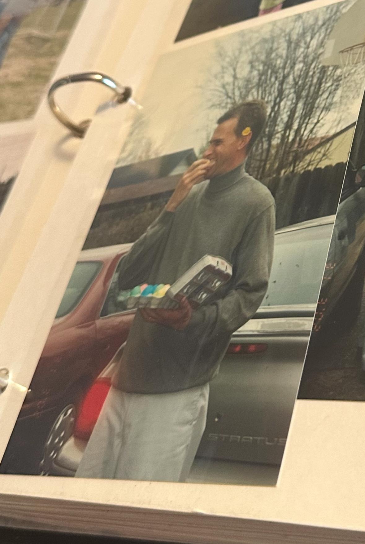 A young man holds snacks in one hand and smiles while standing by a parked car.