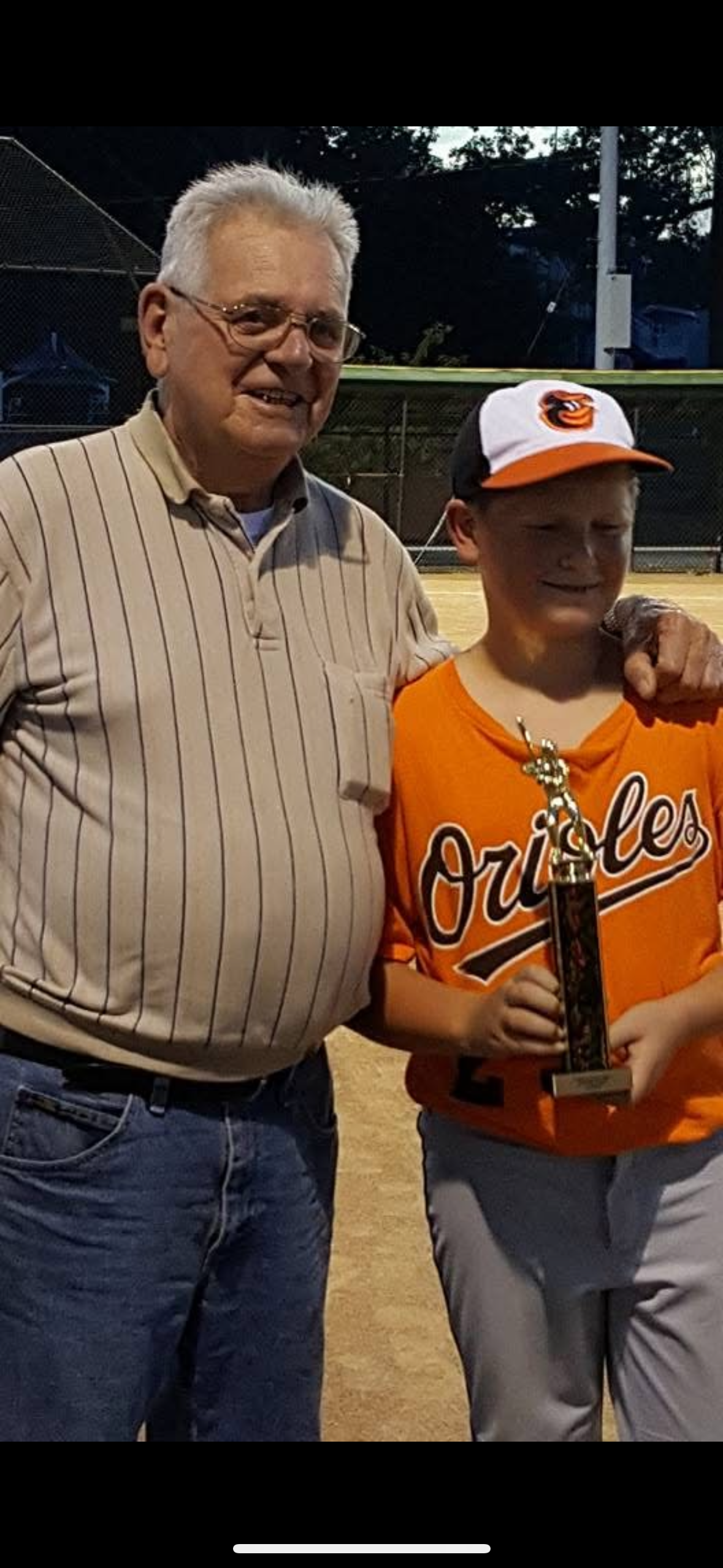 A young boy proudly holds a trophy next to an older man after a baseball game celebration.