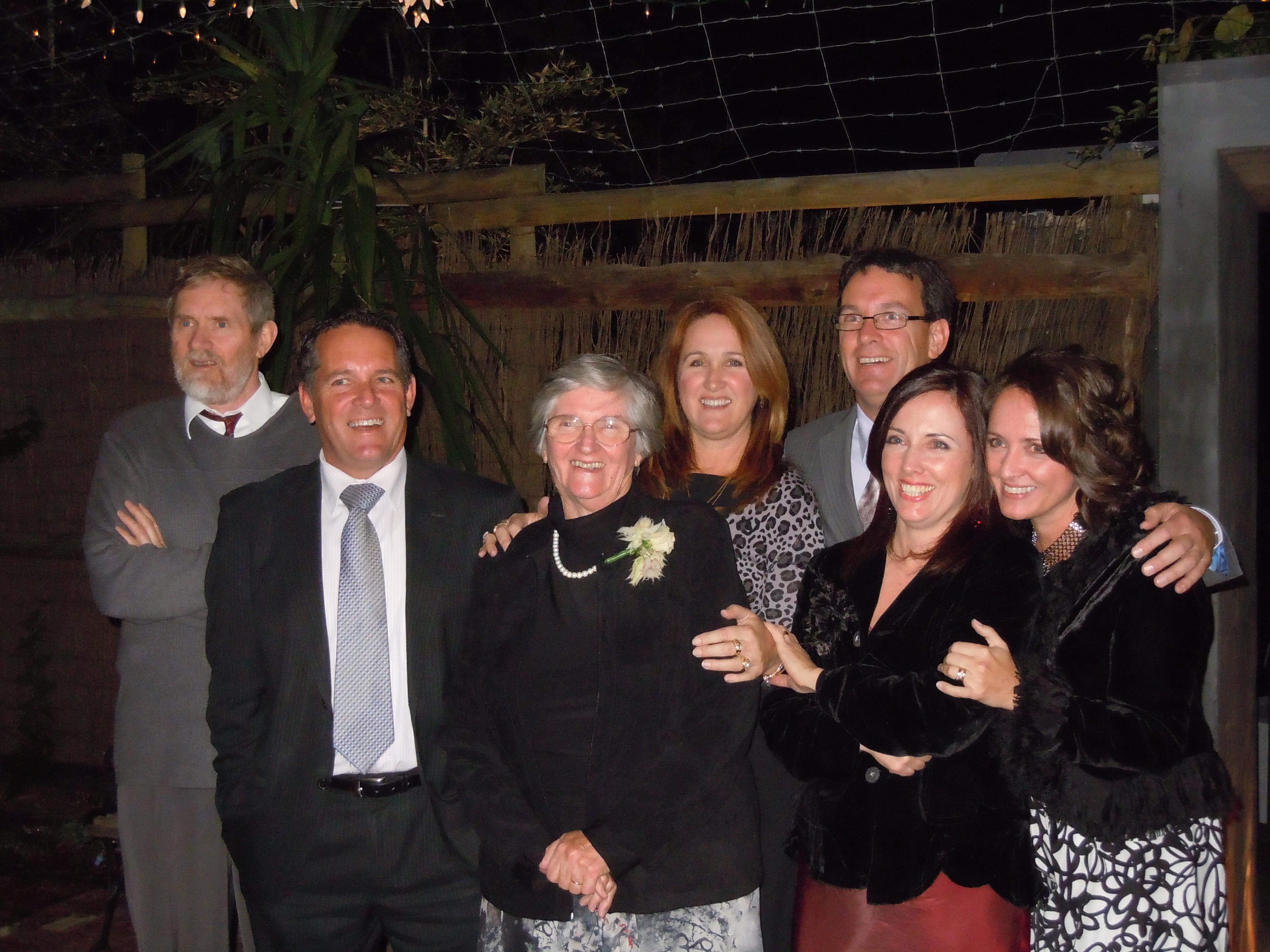 A group of seven people poses cheerfully outside at night, celebrating a special event together.