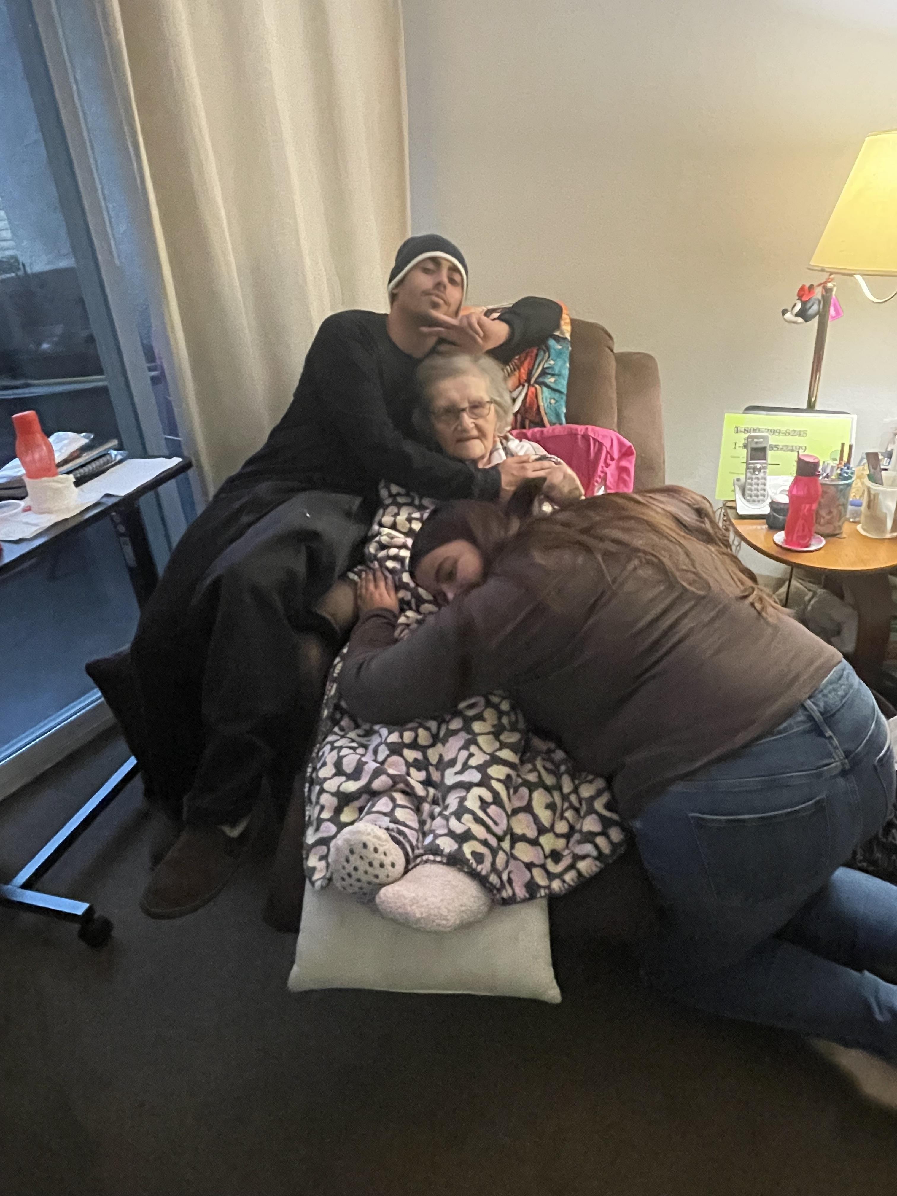 Three family members are sharing a warm moment together on a couch, smiling and relaxed.