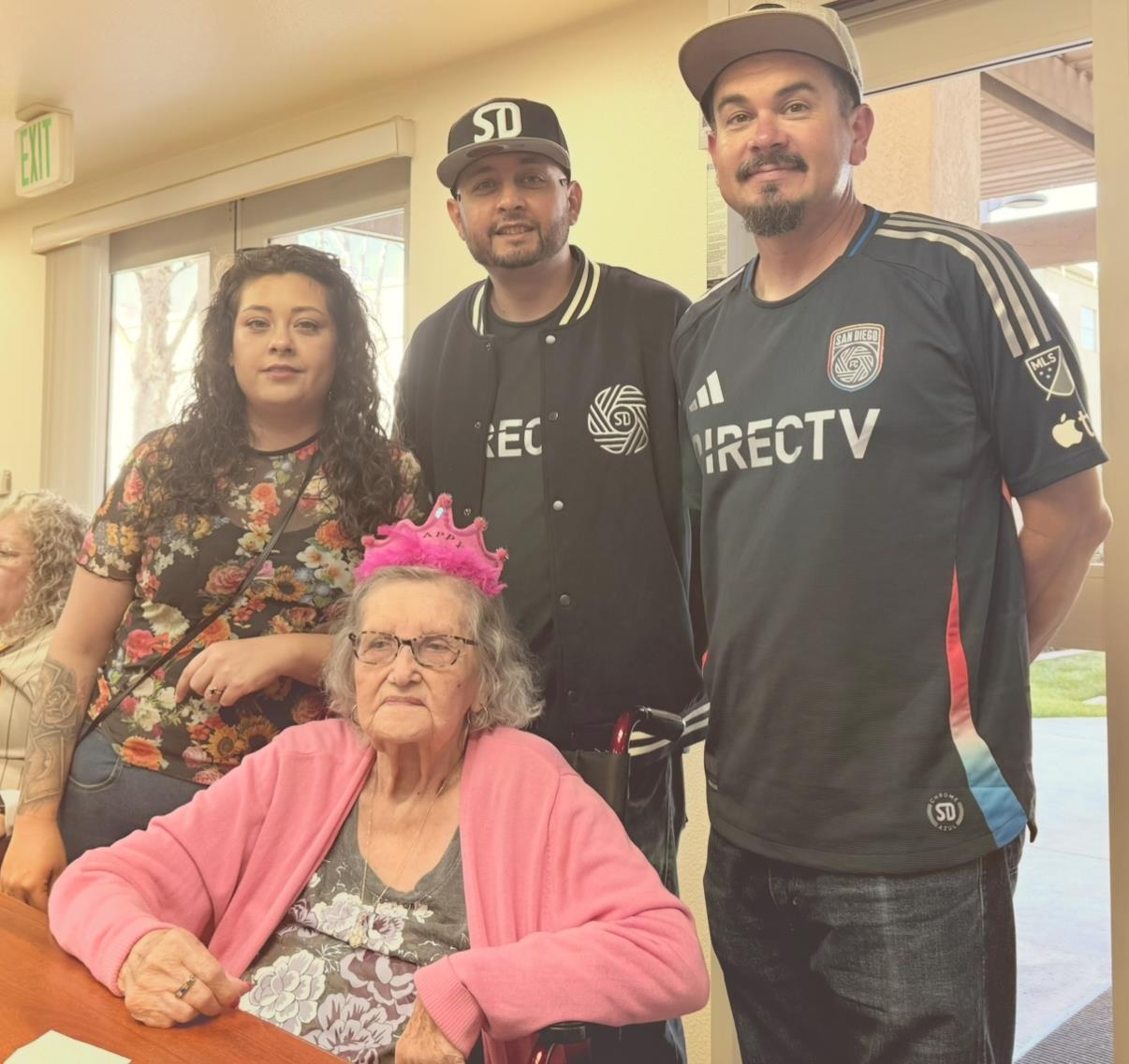 Family members gather to celebrate and enjoy quality time with an elderly woman at a care facility.