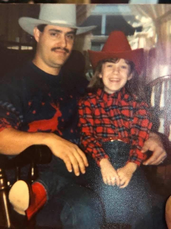 A smiling father and daughter wear cowgirl outfits while sitting together at a festive gathering.