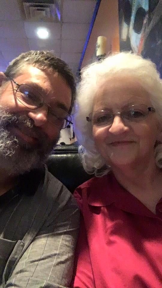 Two individuals are smiling as they enjoy each other's company at a cafe.