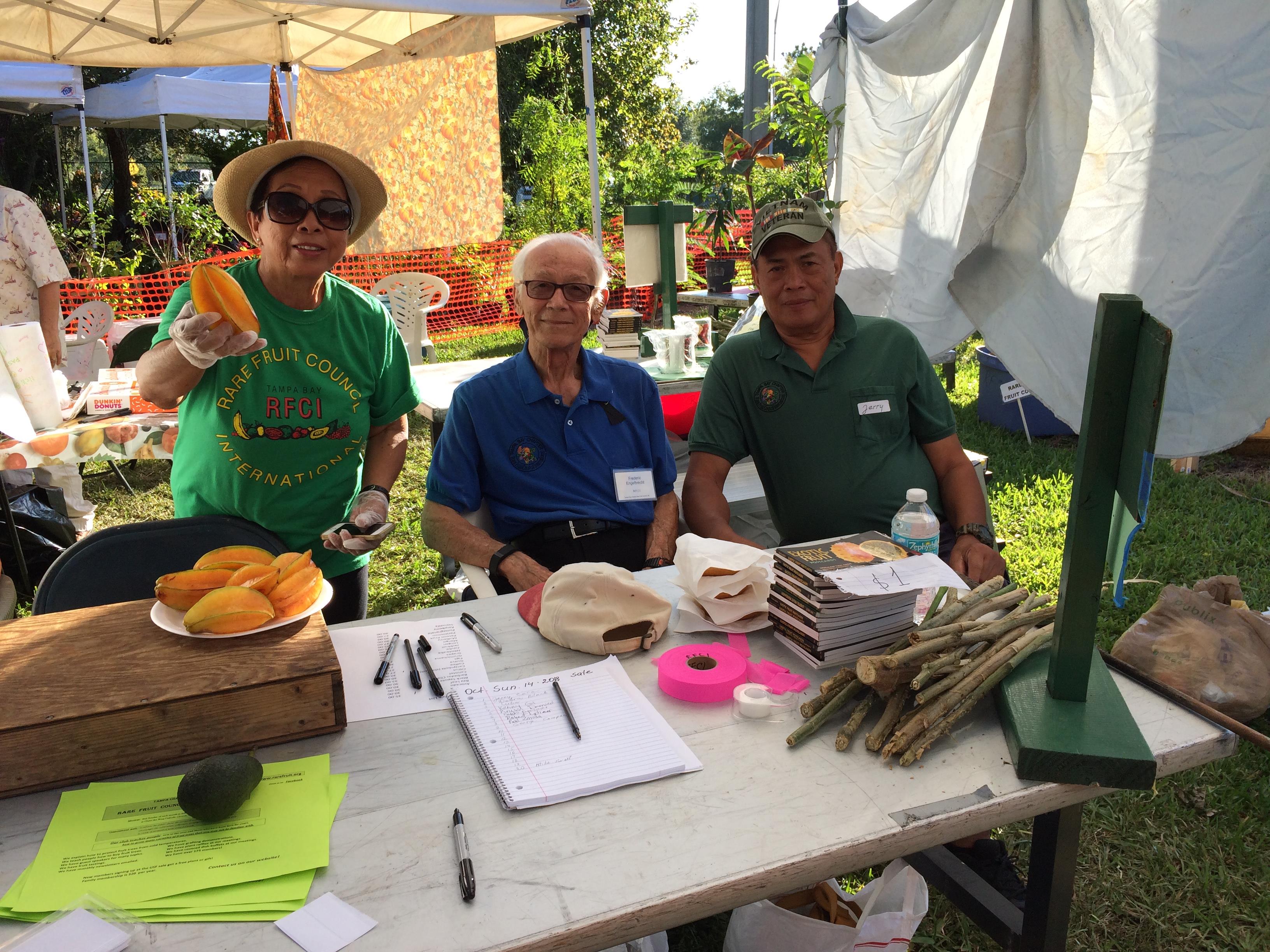 Three people serve food and engage with attendees at a lively local event.