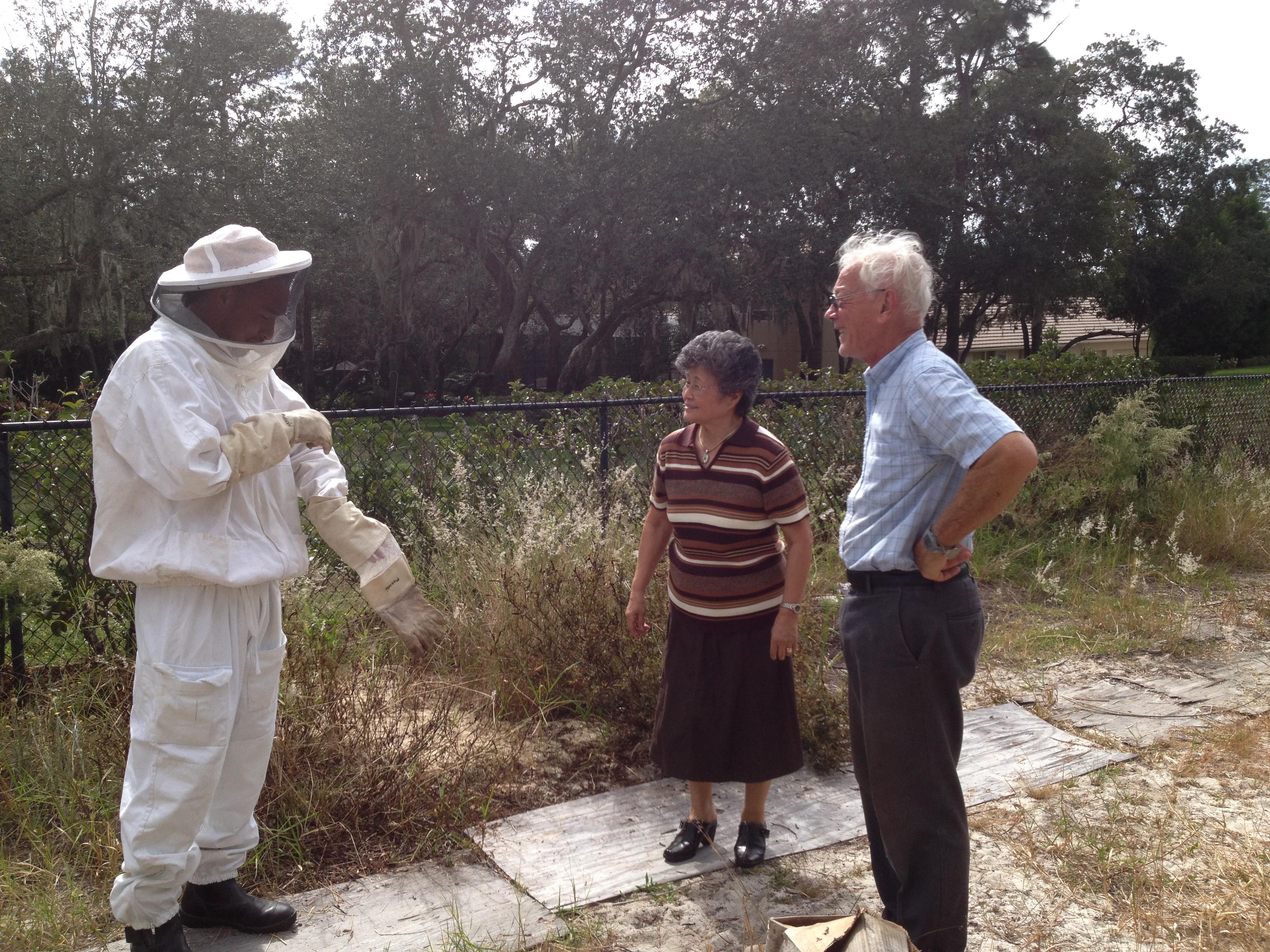Elderly couple engages with a beekeeper who explains proper techniques and safety gear.