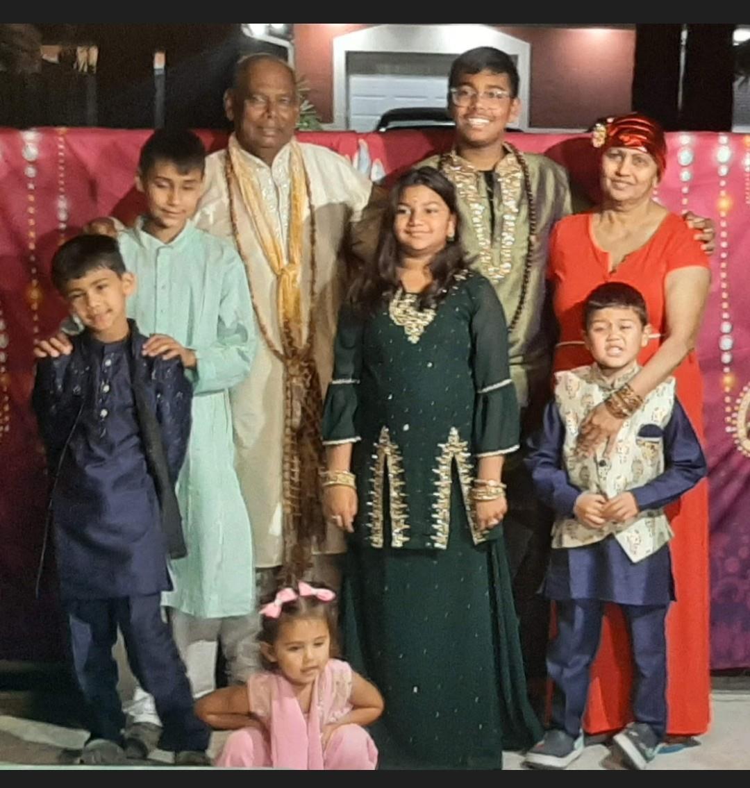 A group of family members poses in traditional clothing, smiling, during a festive gathering.