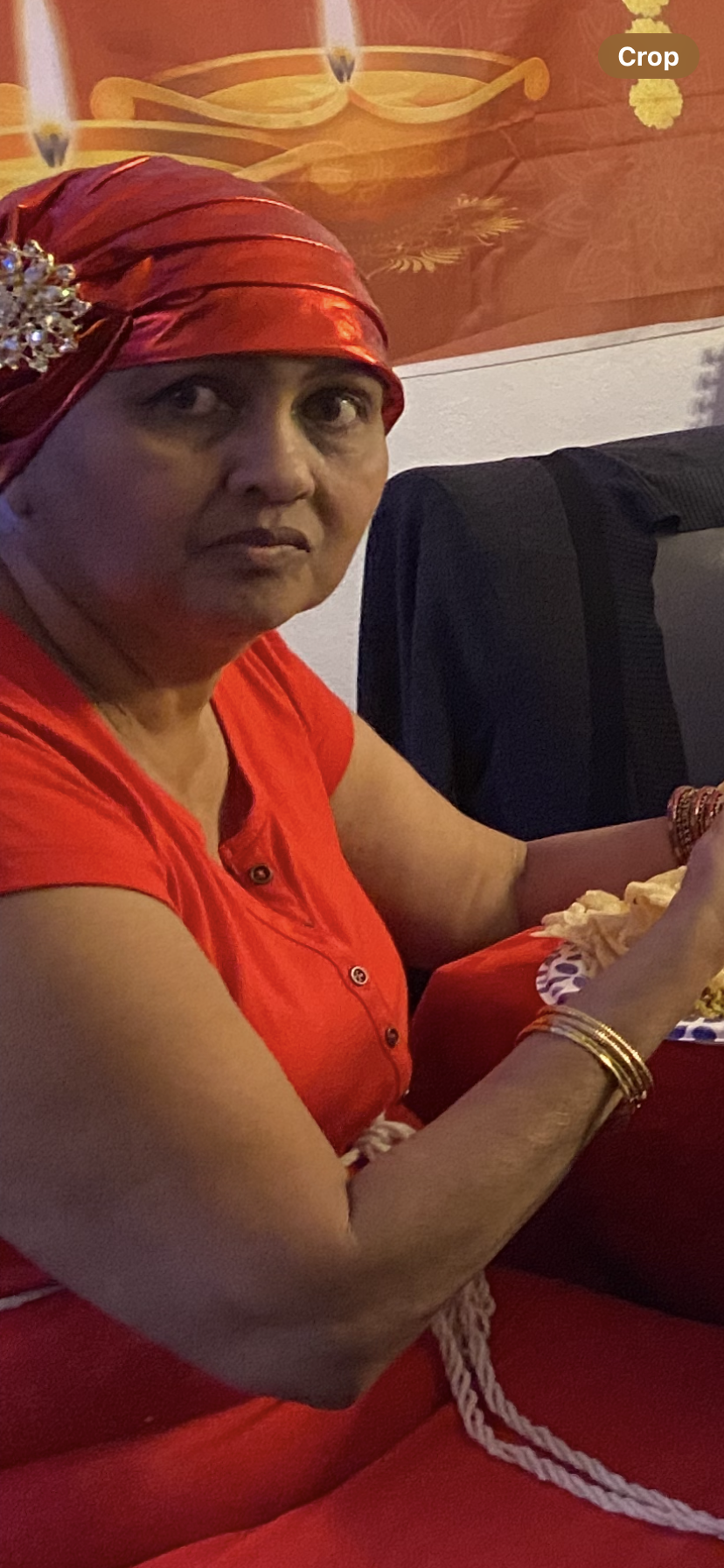 An elderly woman in a red shirt happily enjoys snacks at a gathering.