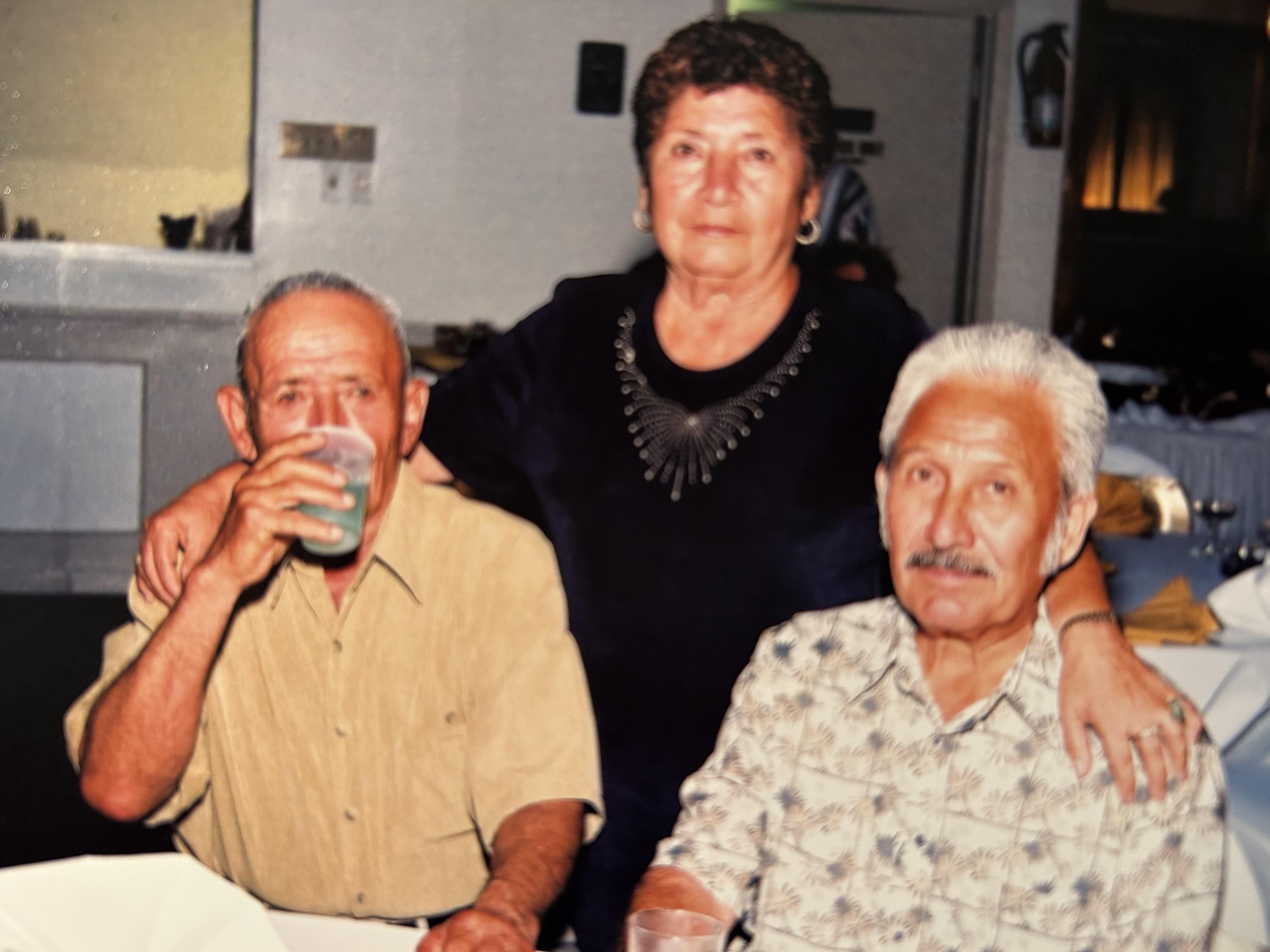 A warm gathering captures three older adults enjoying each other's company and drinks.