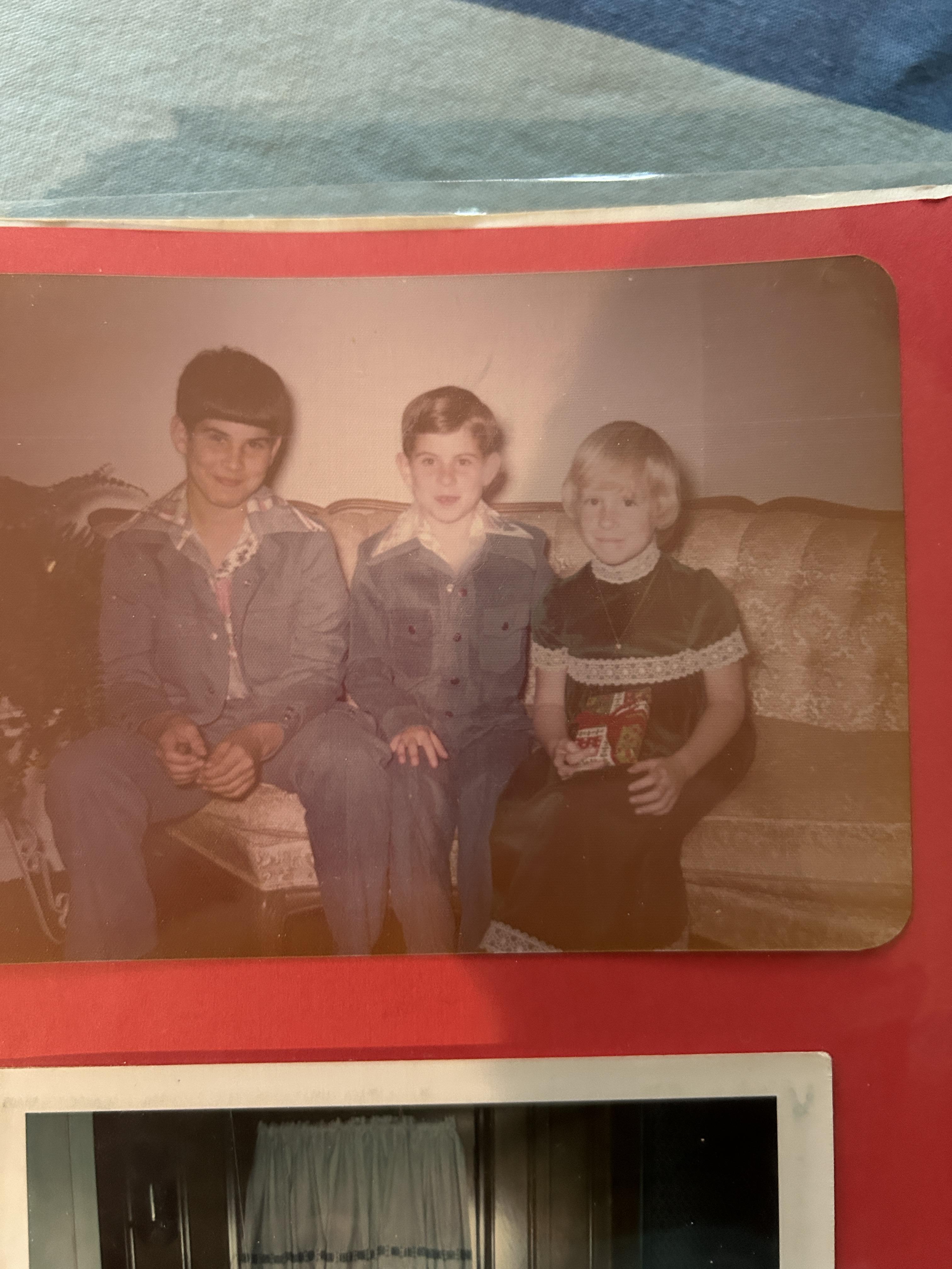 Three children sit close together on a couch in a vintage living room setting.