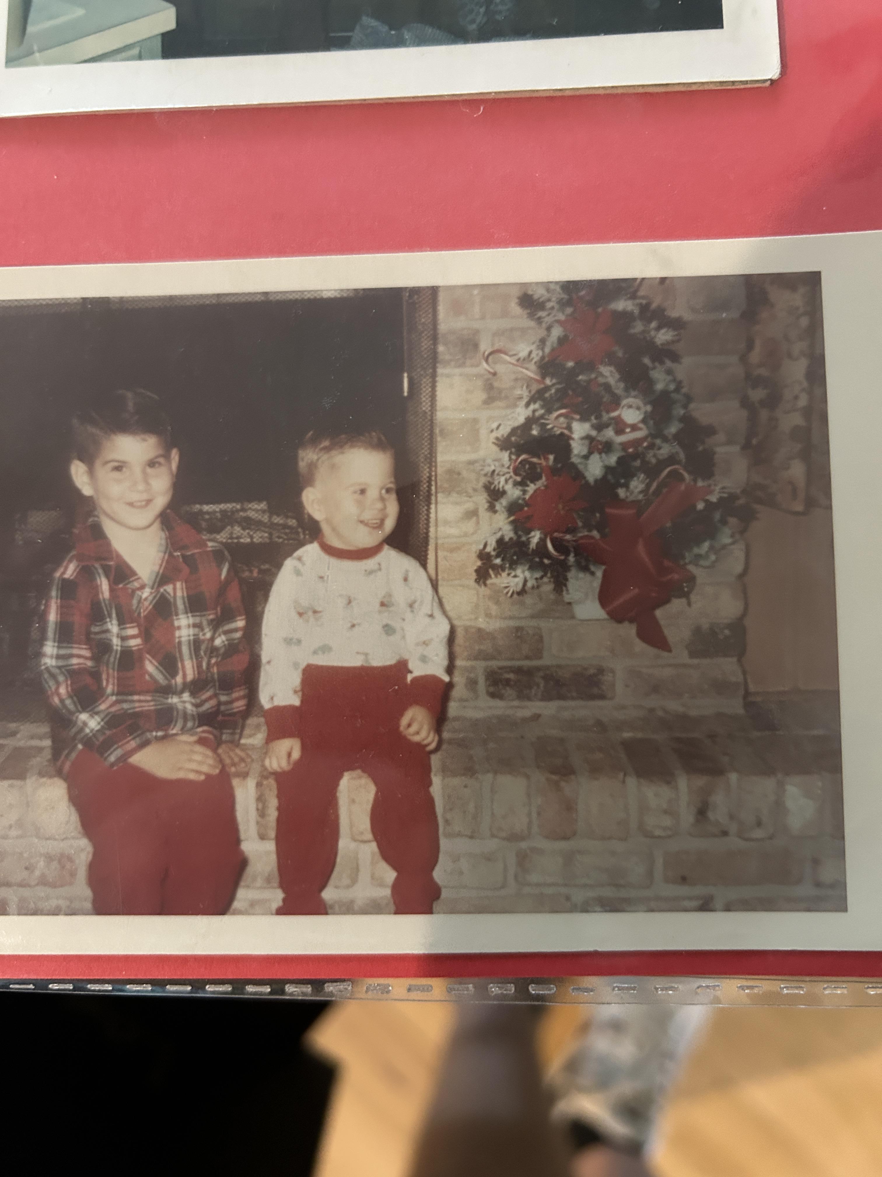 Two young boys smile while sitting on a brick hearth, surrounded by holiday decorations and cheer.