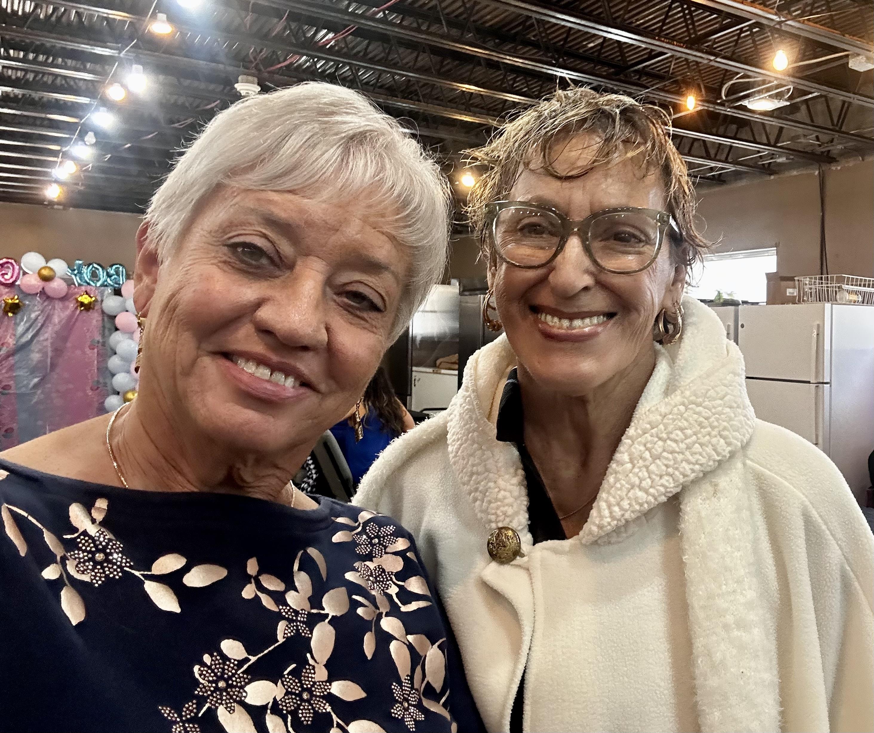 Two women pose happily, showcasing their friendship at a vibrant indoor gathering.