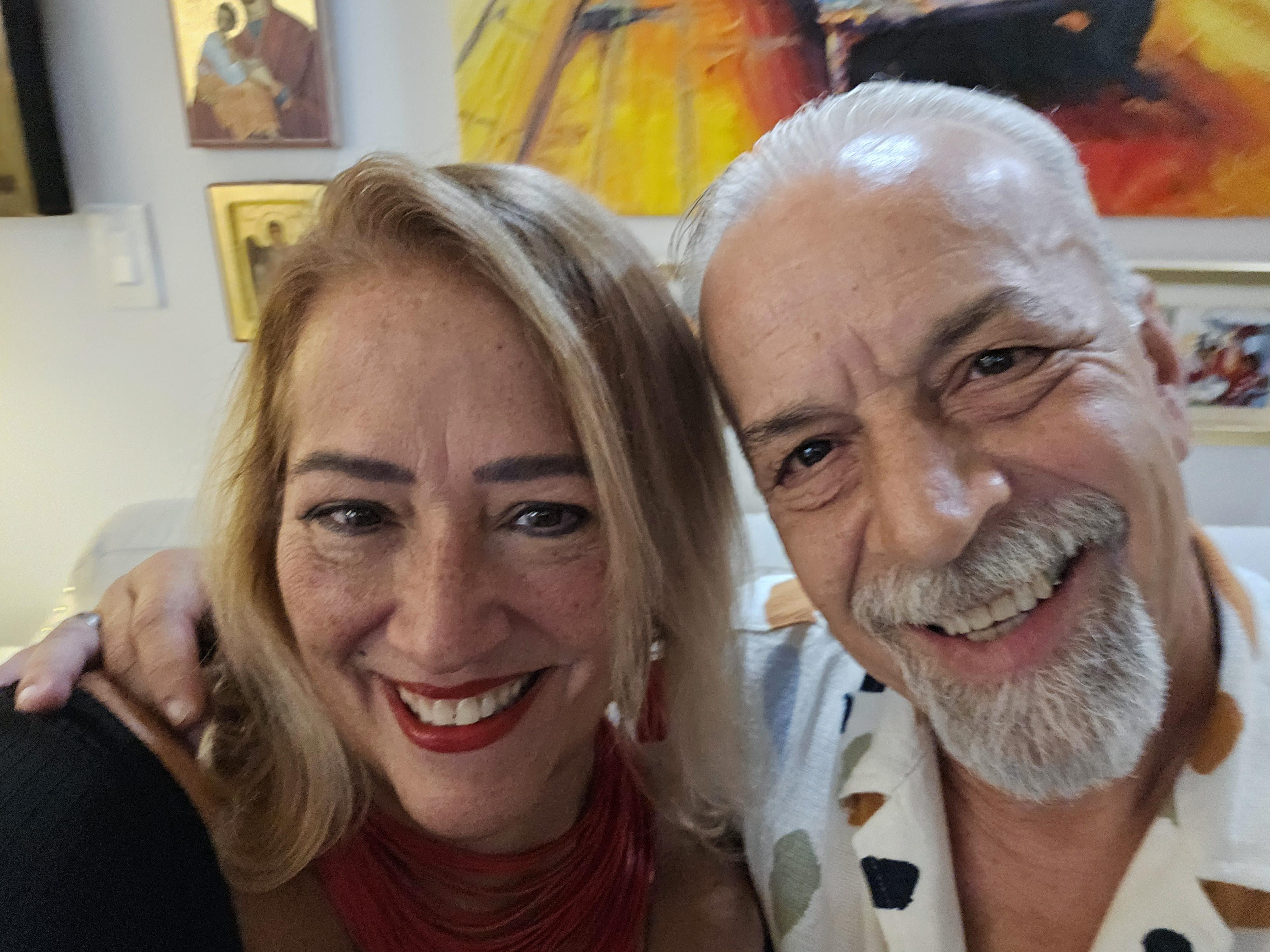 Two friends pose happily together in an art gallery filled with colorful artwork.