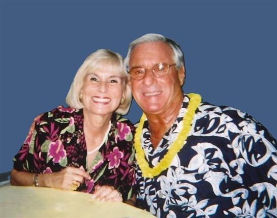 Happy couple poses in bright floral outfits at a lively tropical-themed event.