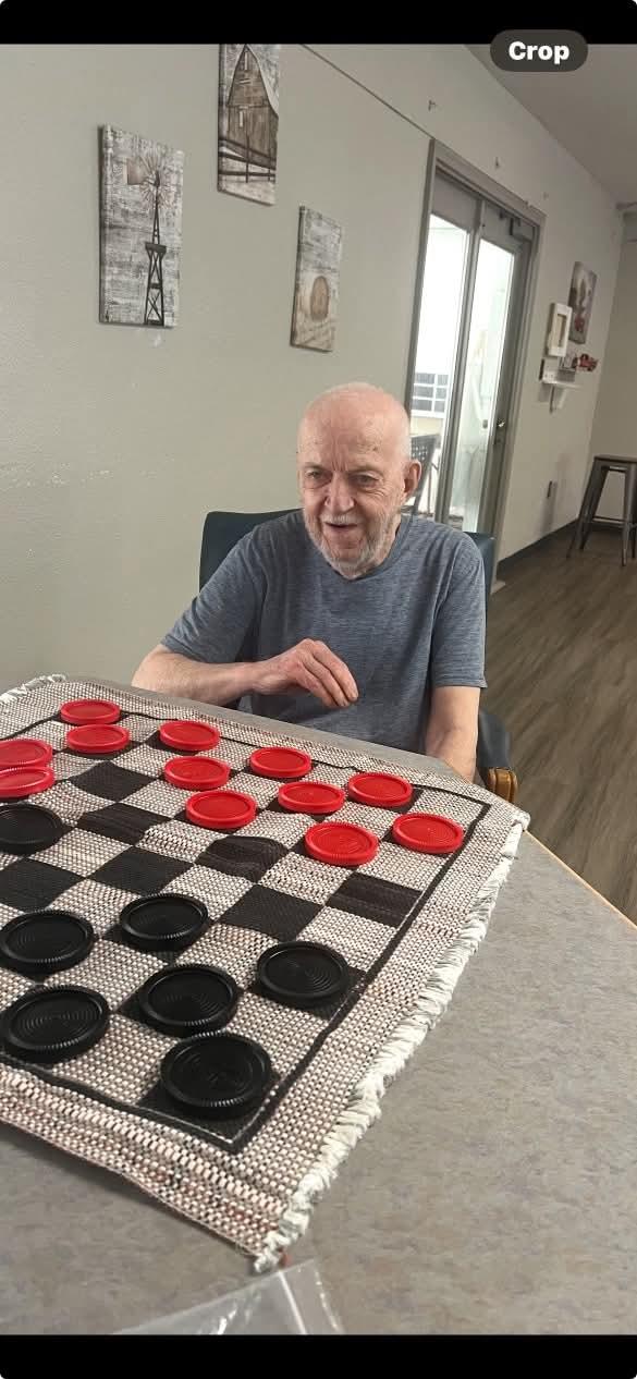 A senior man focuses on his game of checkers in a bright, comfortable care facility setting.
