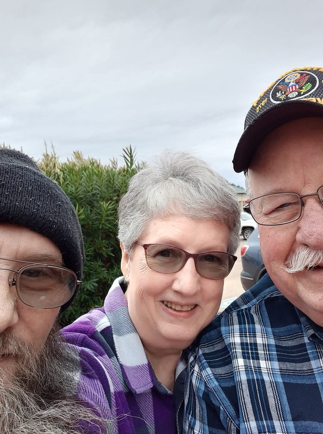 Three family members smile and pose closely together, enjoying a lighthearted moment outdoors.