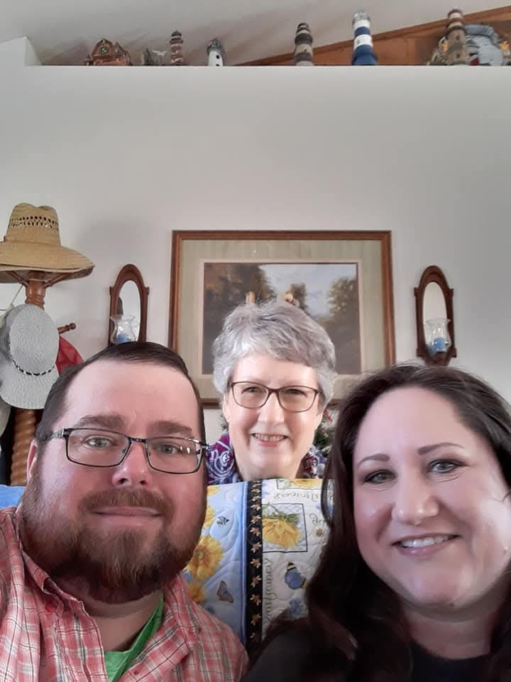 Three family members happily pose together in a warm, inviting living room setting.