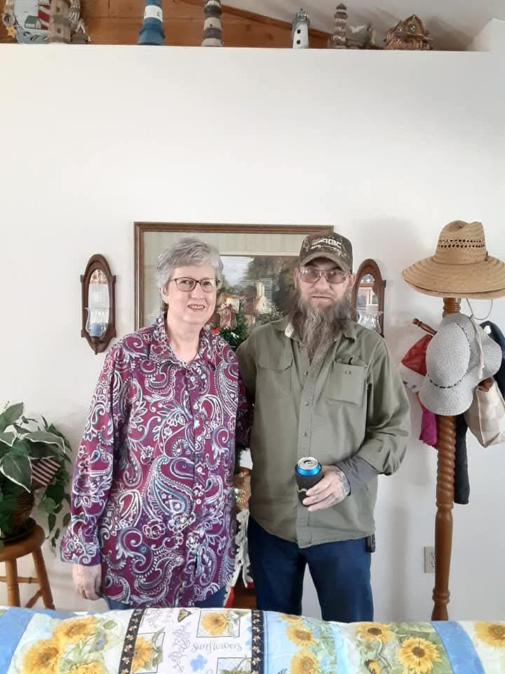 Two people pose together in a cozy indoor setting, smiling and enjoying a casual moment.