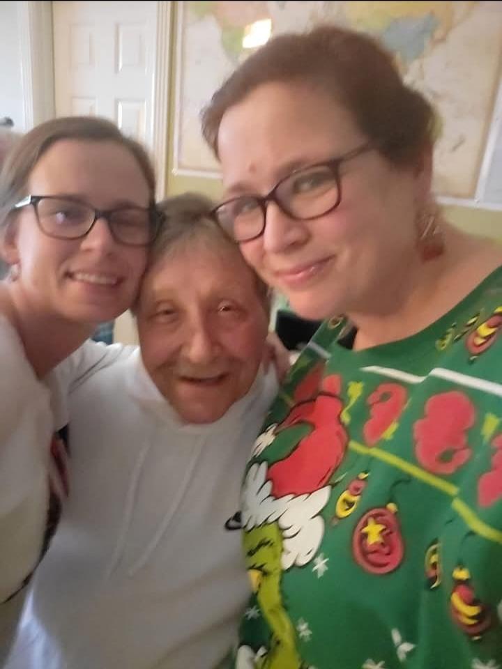Two women embrace their grandmother with smiles in a warm, festive home atmosphere during holidays.