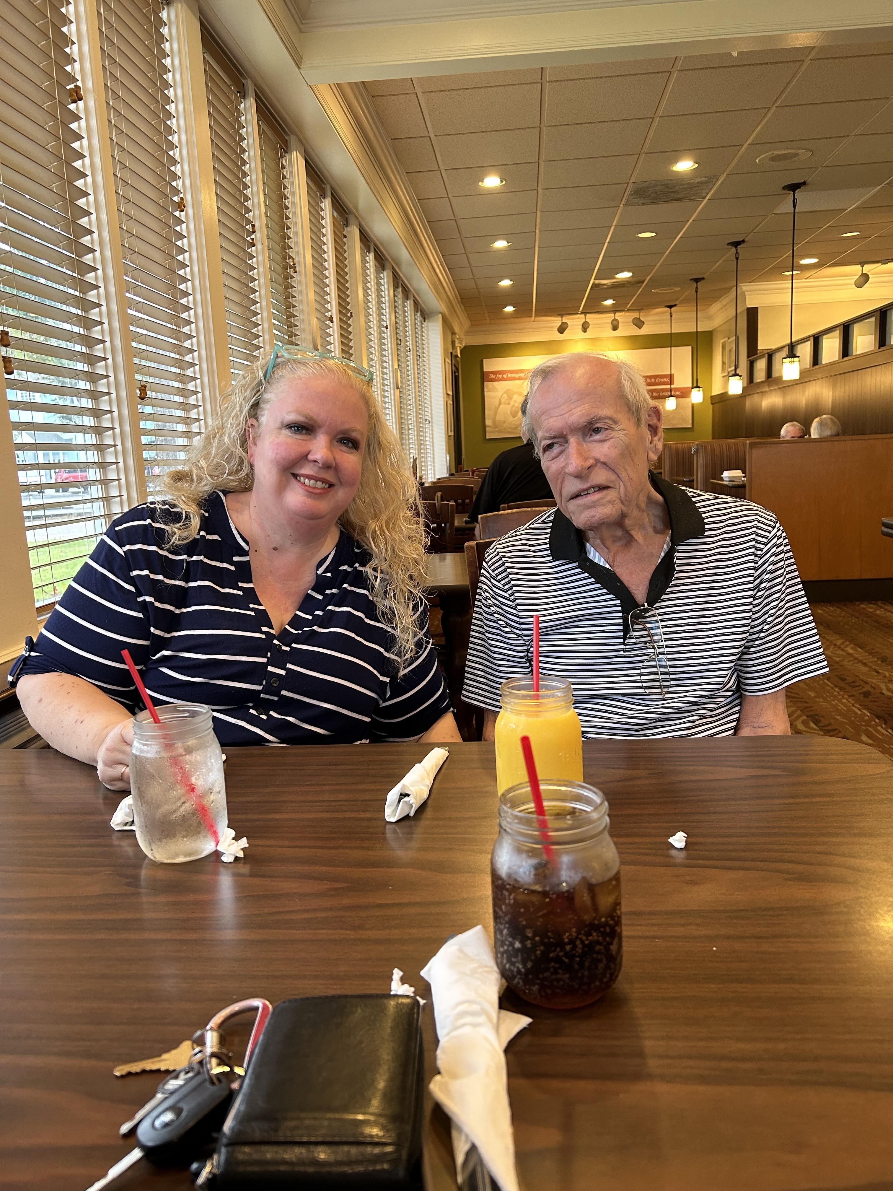 A woman and an older man share a cheerful moment at a table while enjoying their drinks.