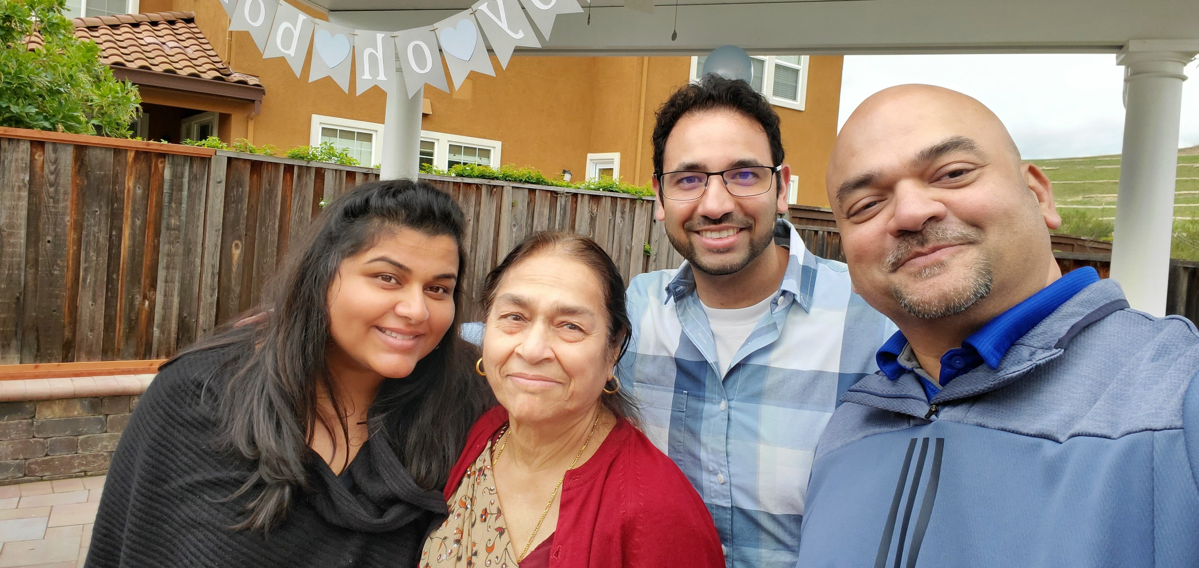 Four family members smile together in a backyard, enjoying their time at a casual celebration.