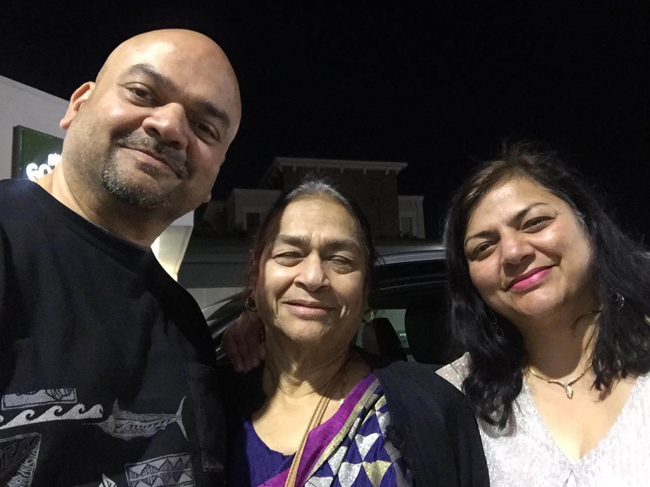 Three adults smile warmly together at nighttime, enjoying each other's company outdoors.