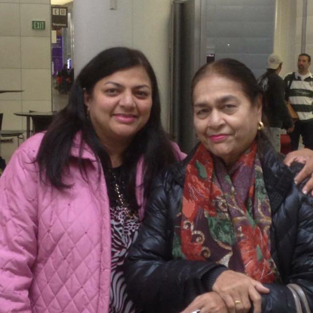 Two women pose for a cheerful picture while surrounded by a bustling crowd indoors.