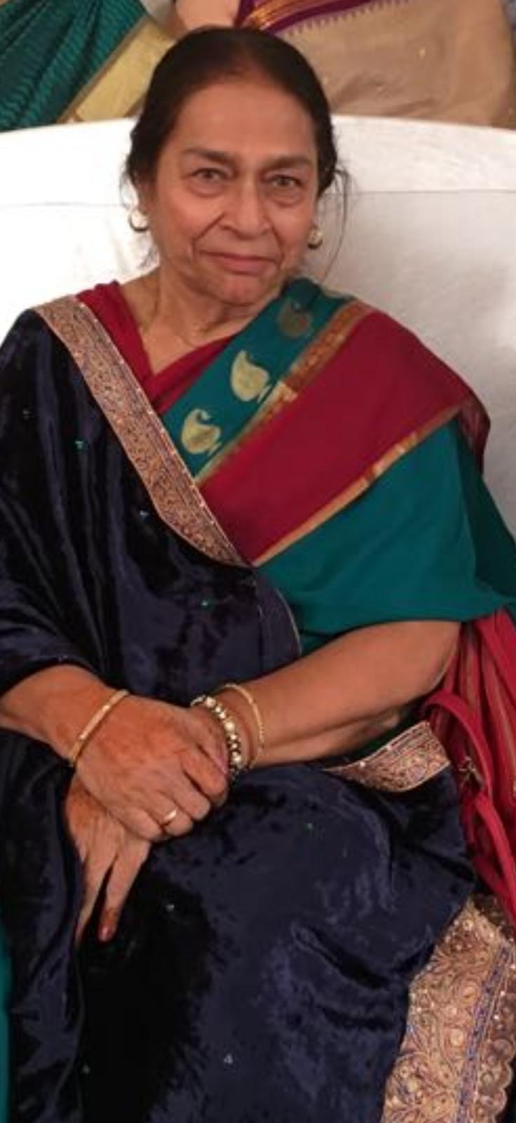 An elderly woman in a colorful saree sits with a serene expression, showcasing her heritage.