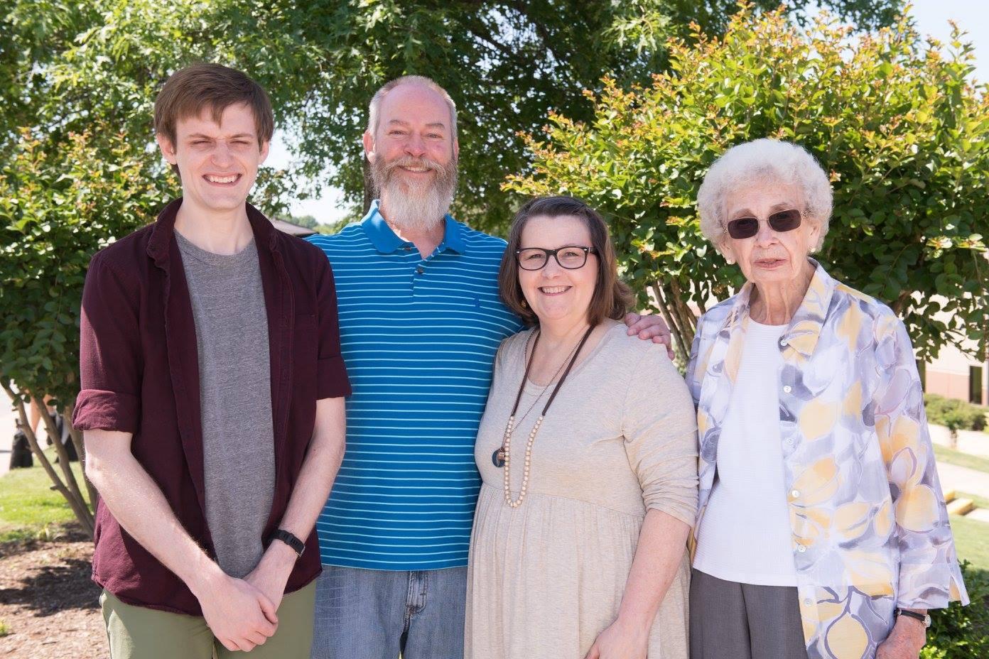 Four family members stand together outside in bright sunlight, smiling and enjoying their time.