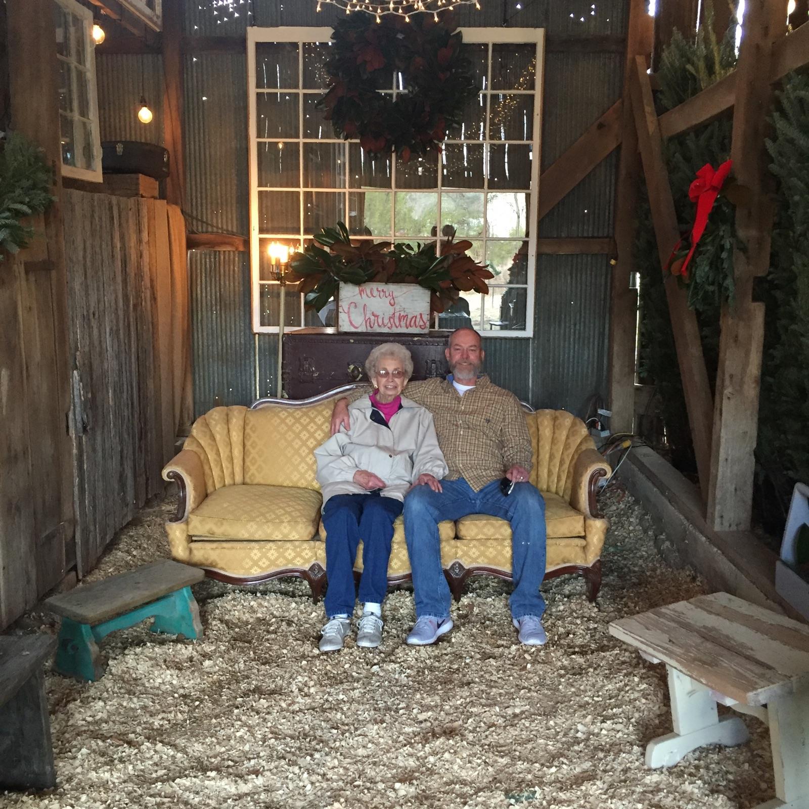 An elderly couple enjoys each other’s company on a cozy couch surrounded by holiday decorations.