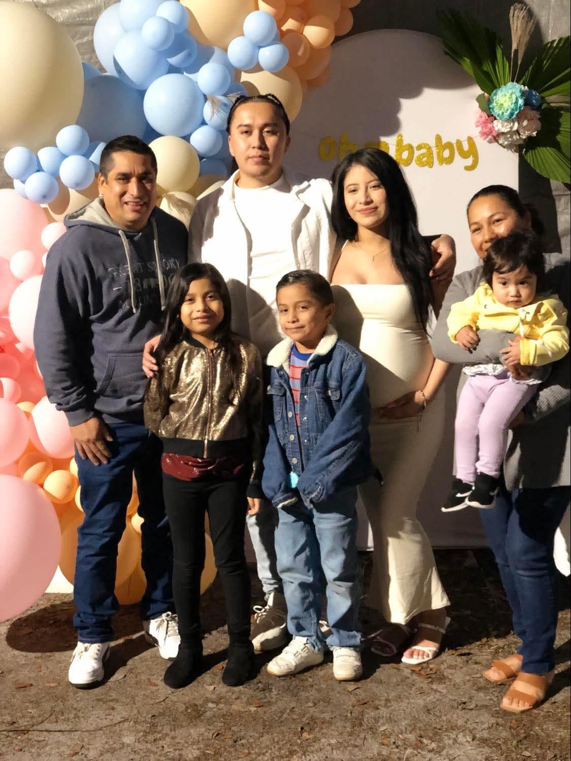 A joyful family poses together in a festive space adorned with balloons celebrating a new baby.