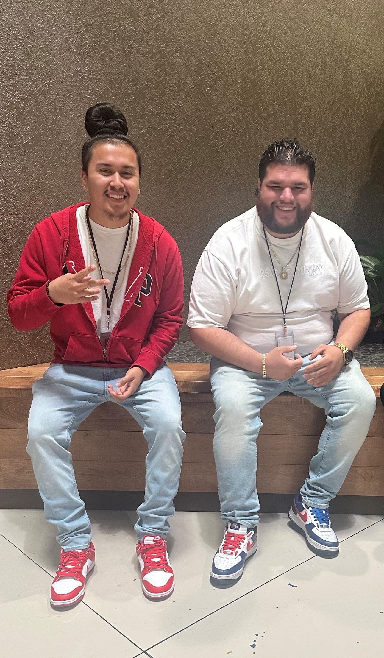 Two friends chat and laugh while sitting on a wooden bench in a casual setting.